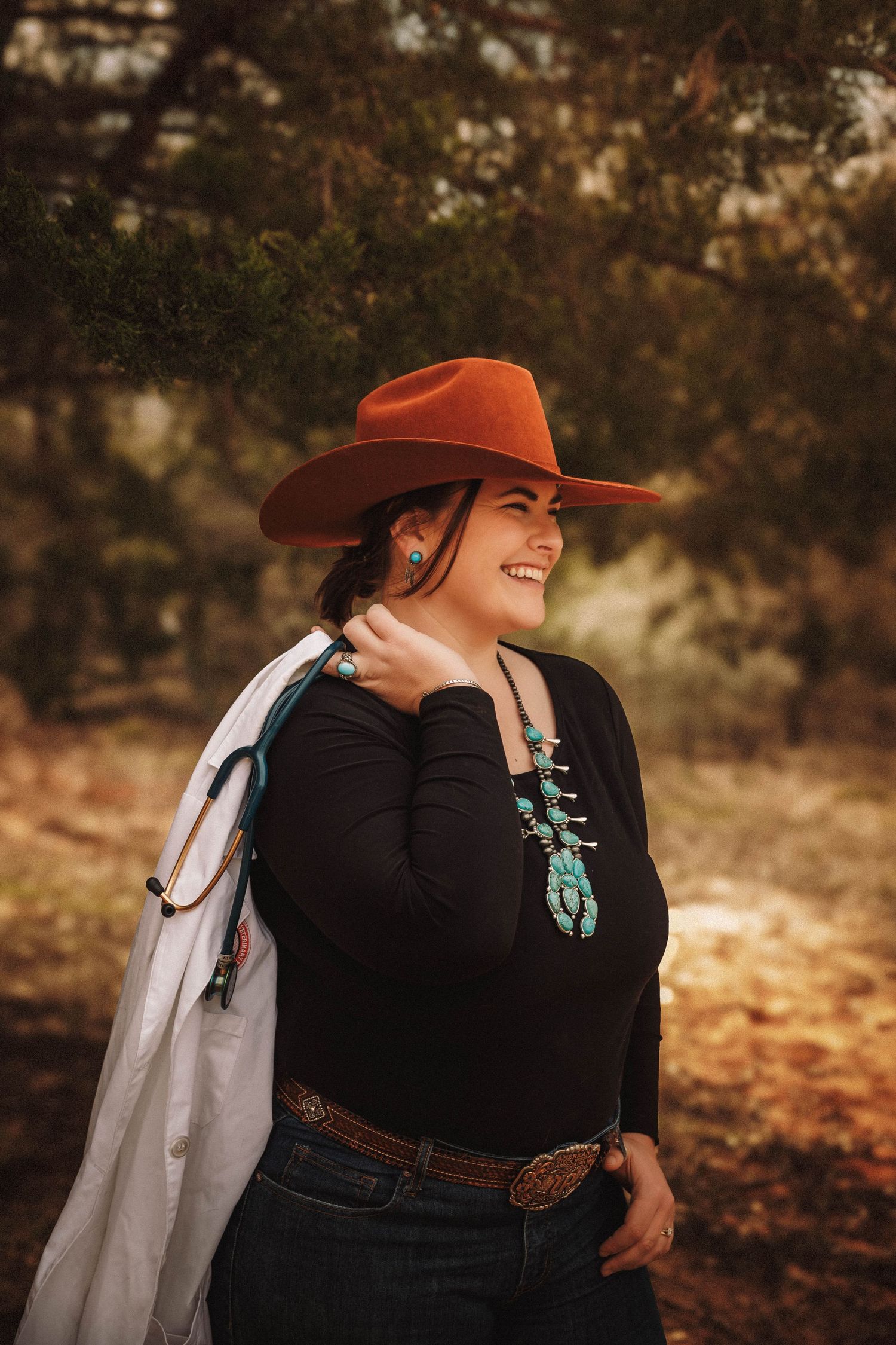 Person wearing a brown cowboy hat and black sweater poses against an autumn woodland backdrop.