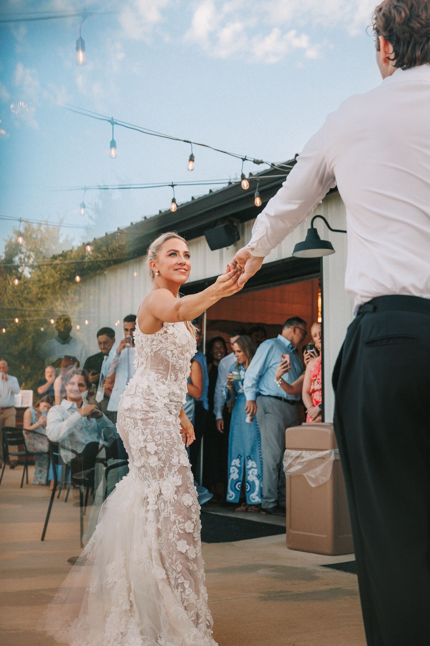A couple dancing together on an outdoor patio with string lights overhead.