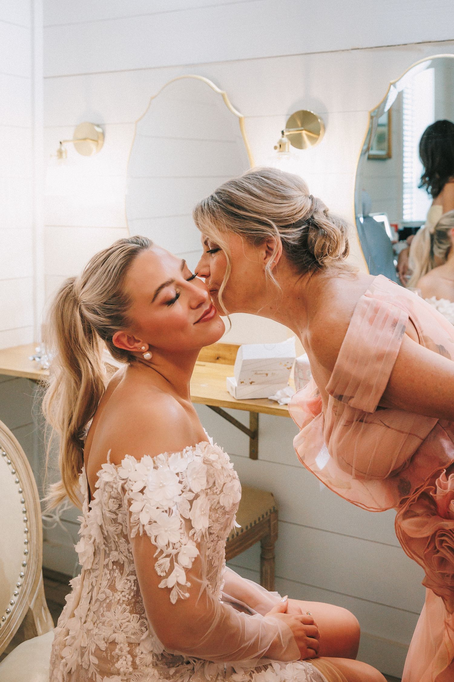 Intimate getting ready moments between loved ones in a bridal suite with white decor and natural lighting.
