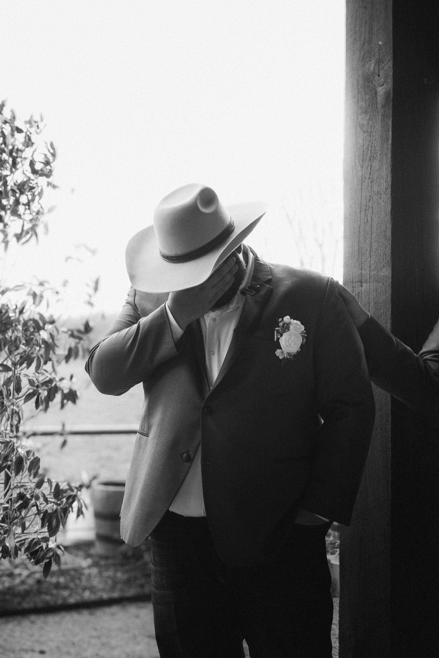 A person in formal attire and cowboy hat leans against a wall in dramatic black and white photography.
