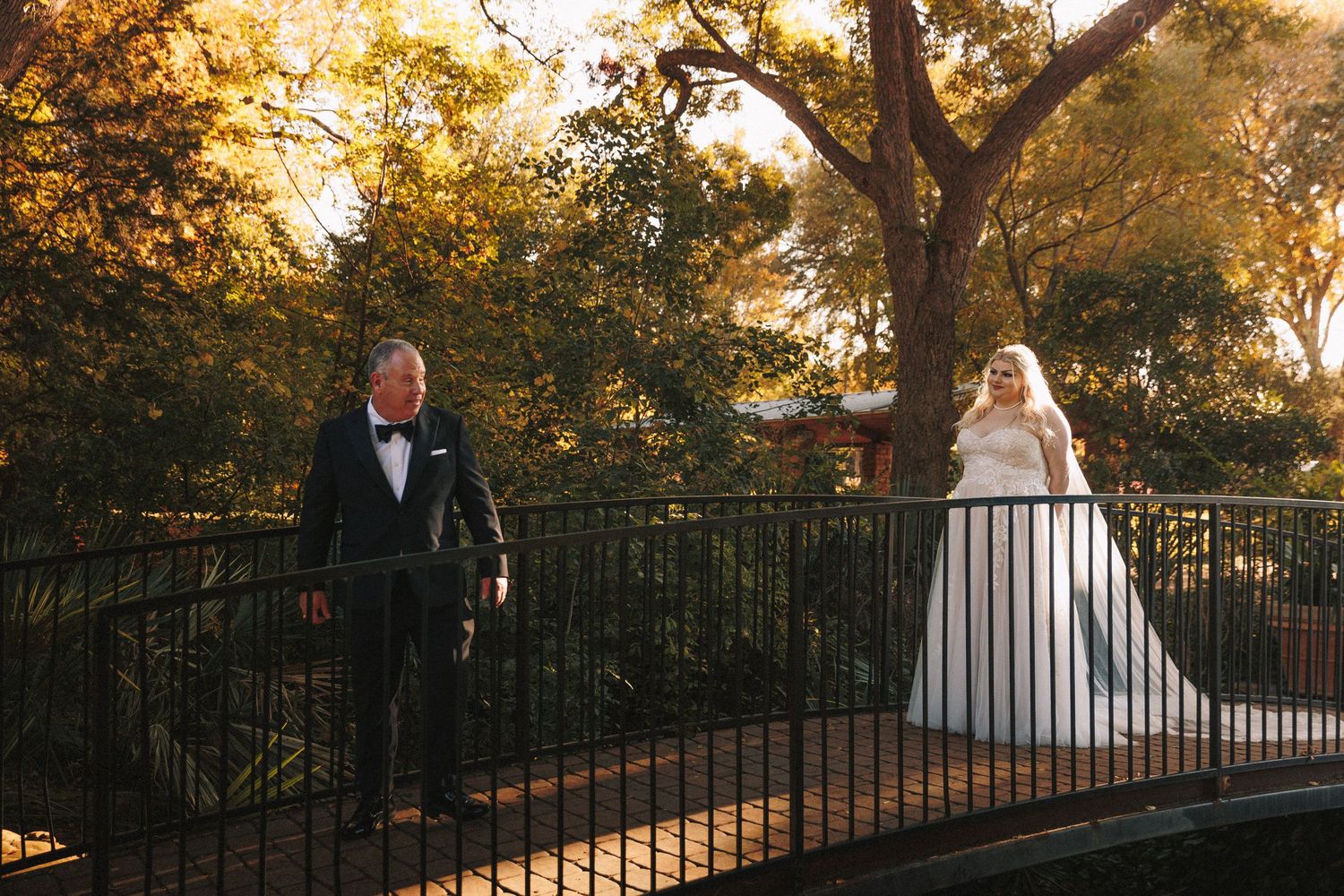 Bride in white gown and groom in tuxedo sharing first look moment on scenic bridge.