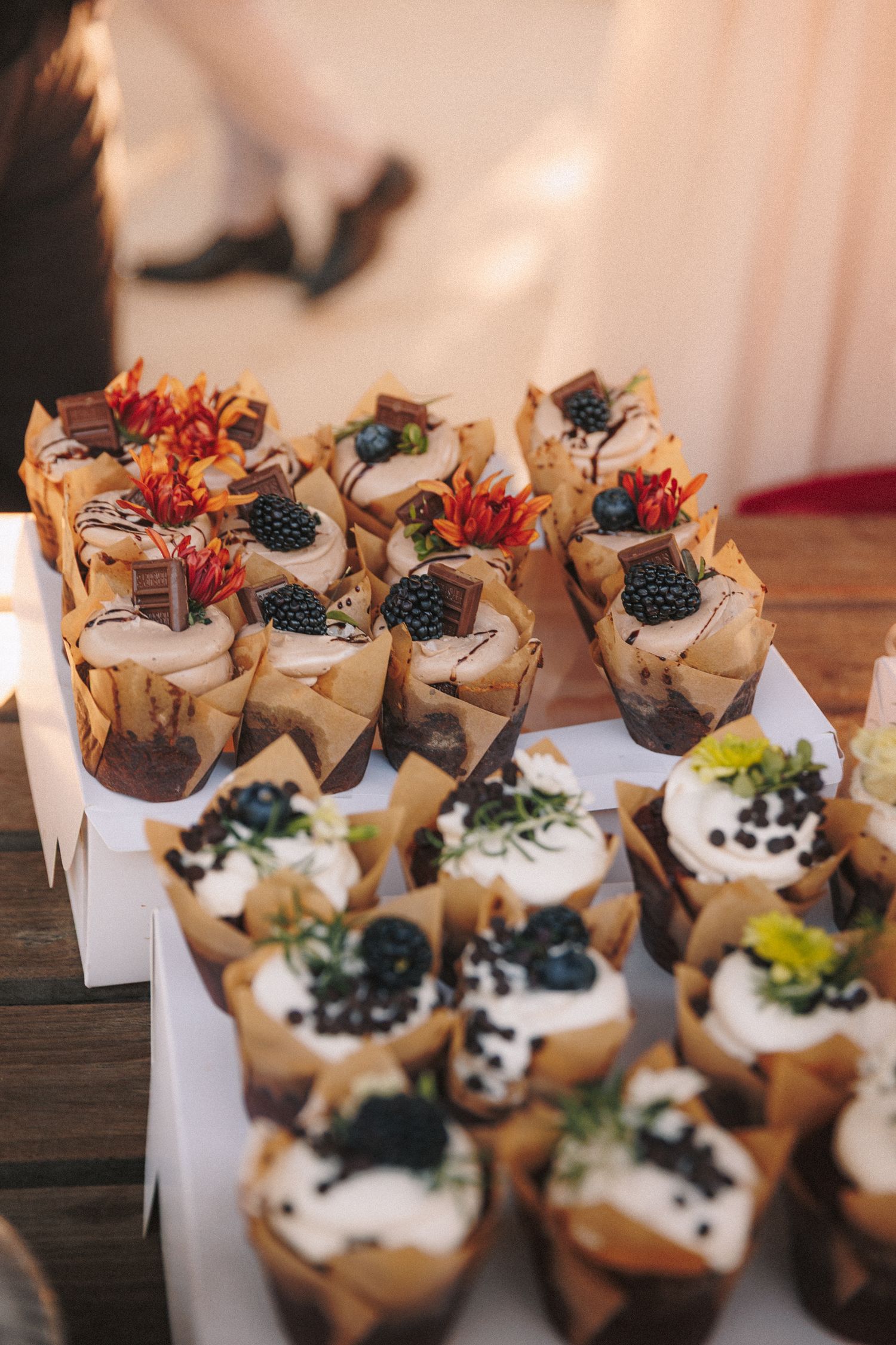 Elegant wedding dessert table featuring decorated cupcakes topped with berries and edible flowers.