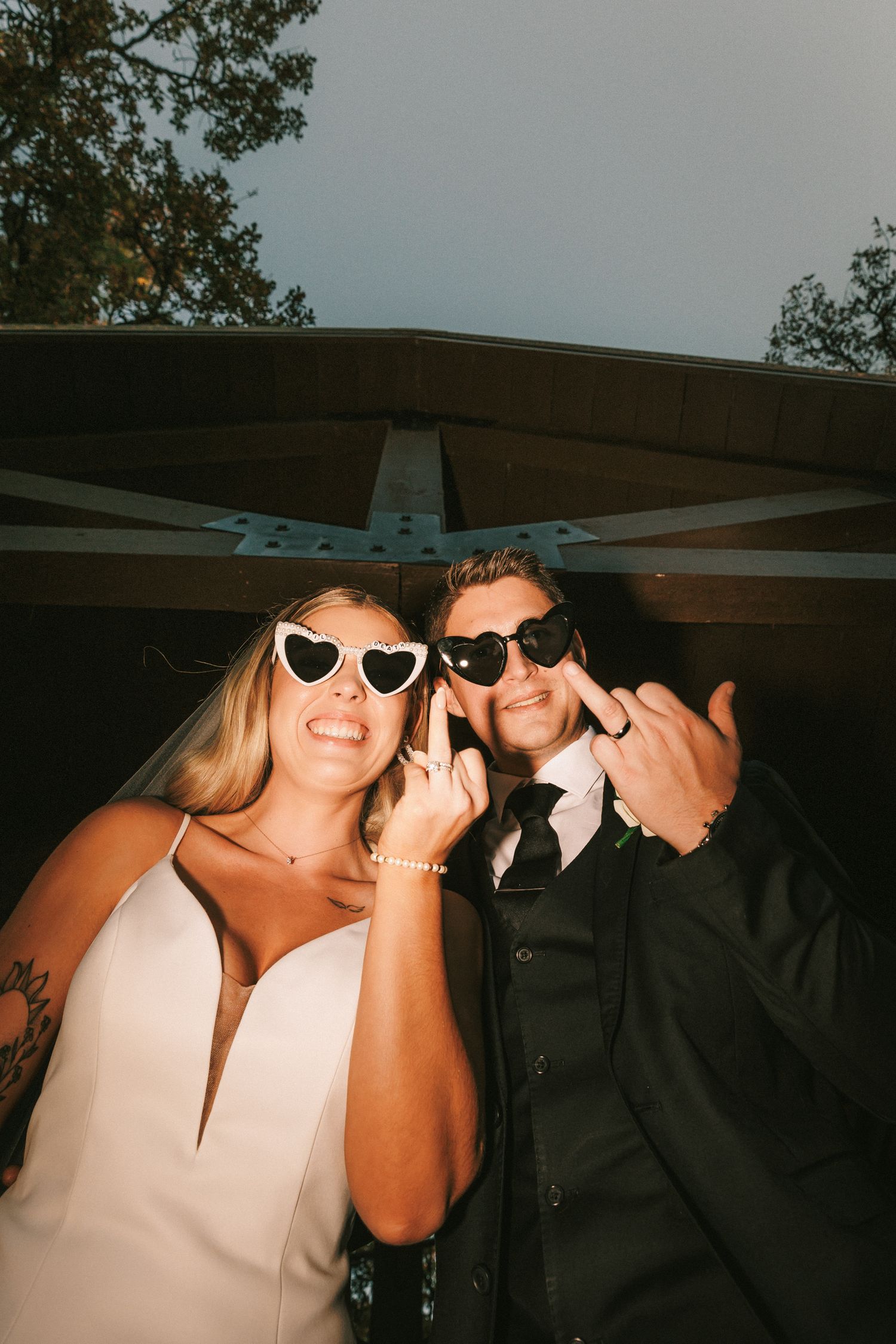 Newlyweds wearing fun sunglasses and smiling at outdoor wedding reception photo booth.