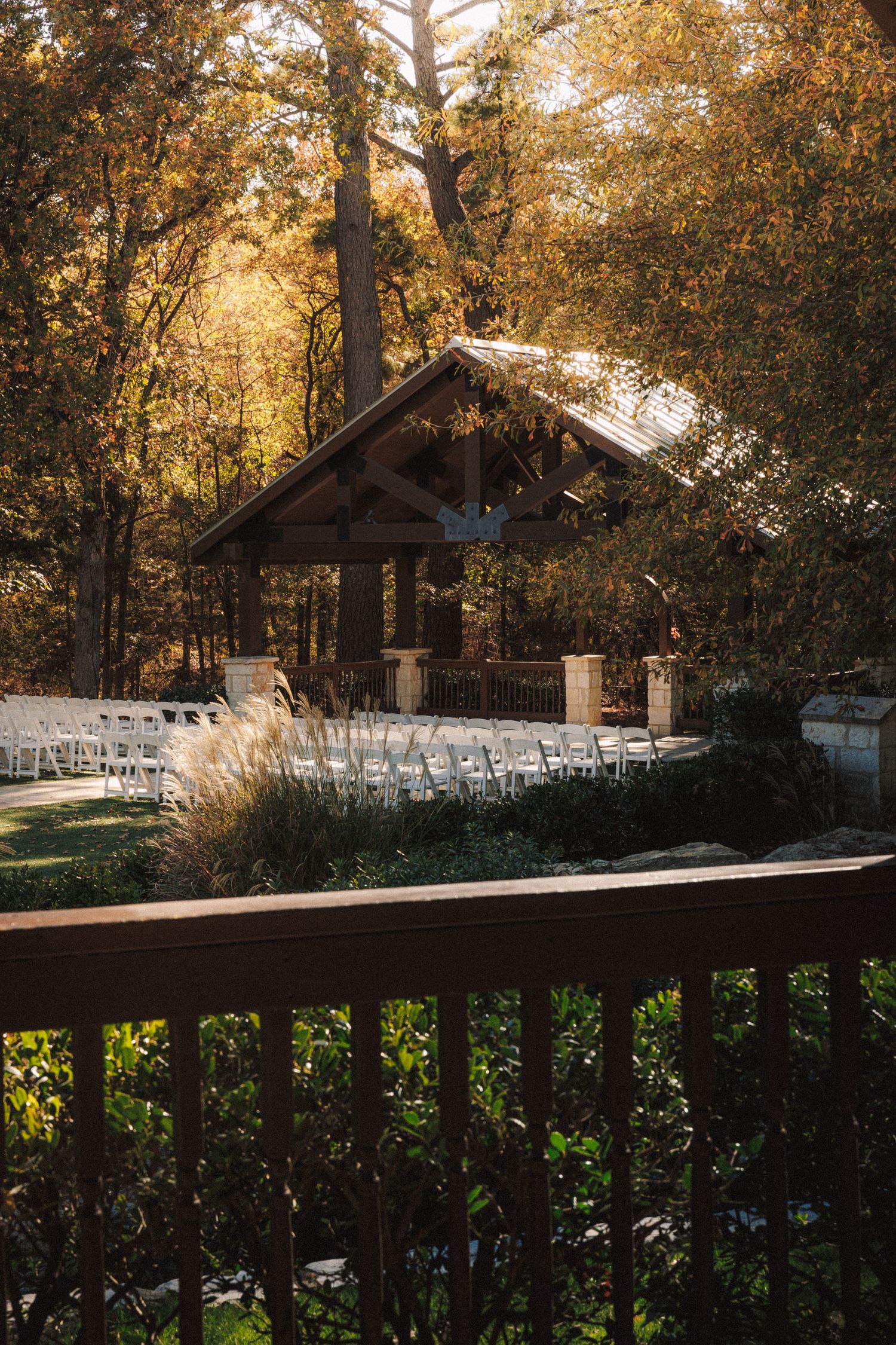 Outdoor wedding ceremony setup with white chairs facing a rustic wooden pavilion in autumn forest.