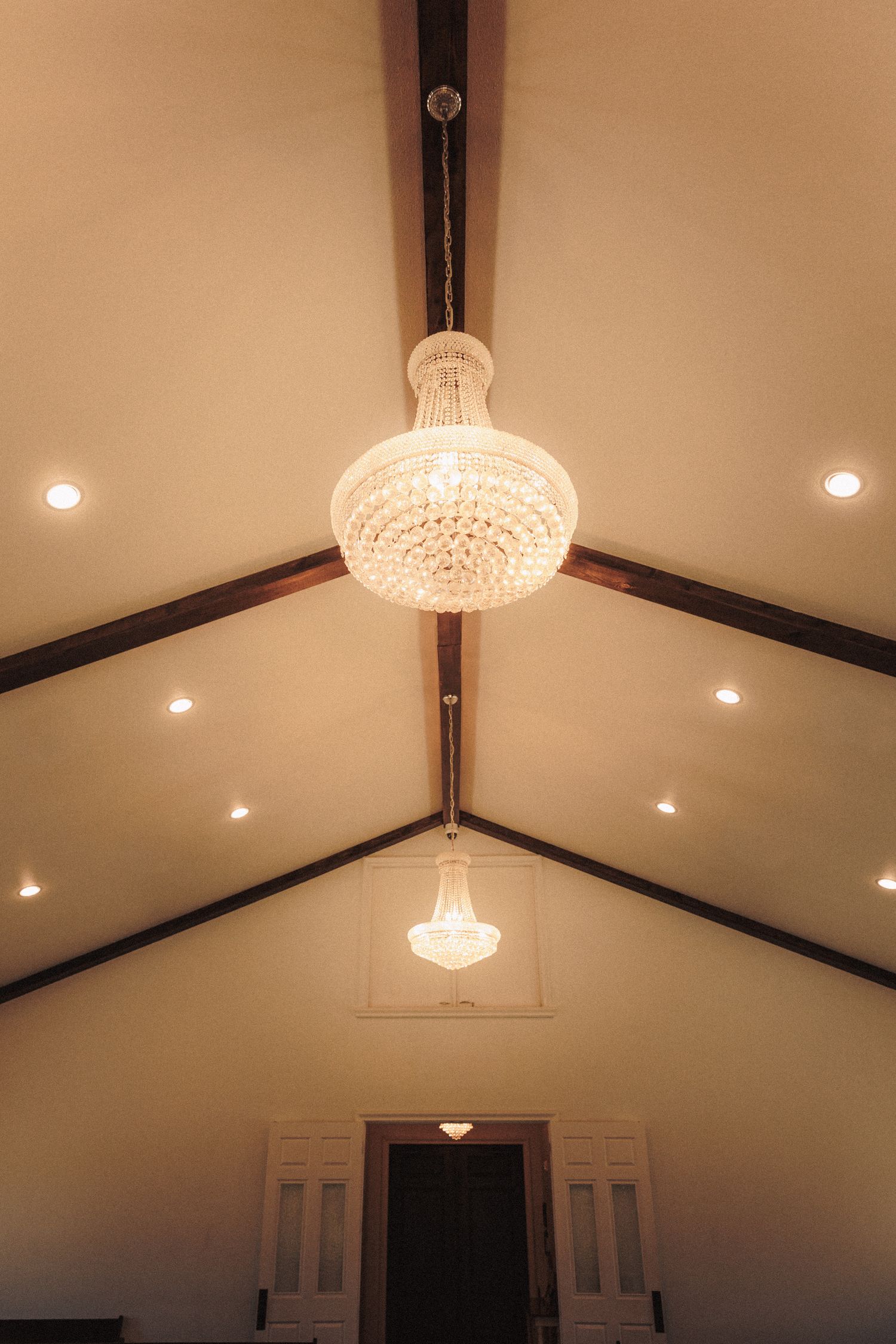 Vaulted ceiling with exposed wood beams and two sparkling crystal chandeliers in a wedding venue chapel.
