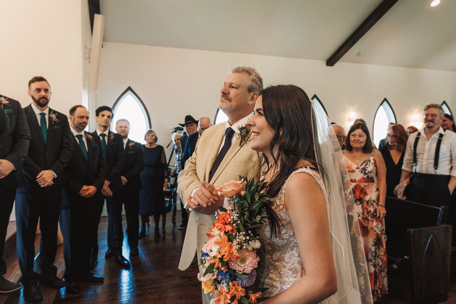 Bride holding colorful bouquet walks down the aisle with her father at a wedding ceremony.