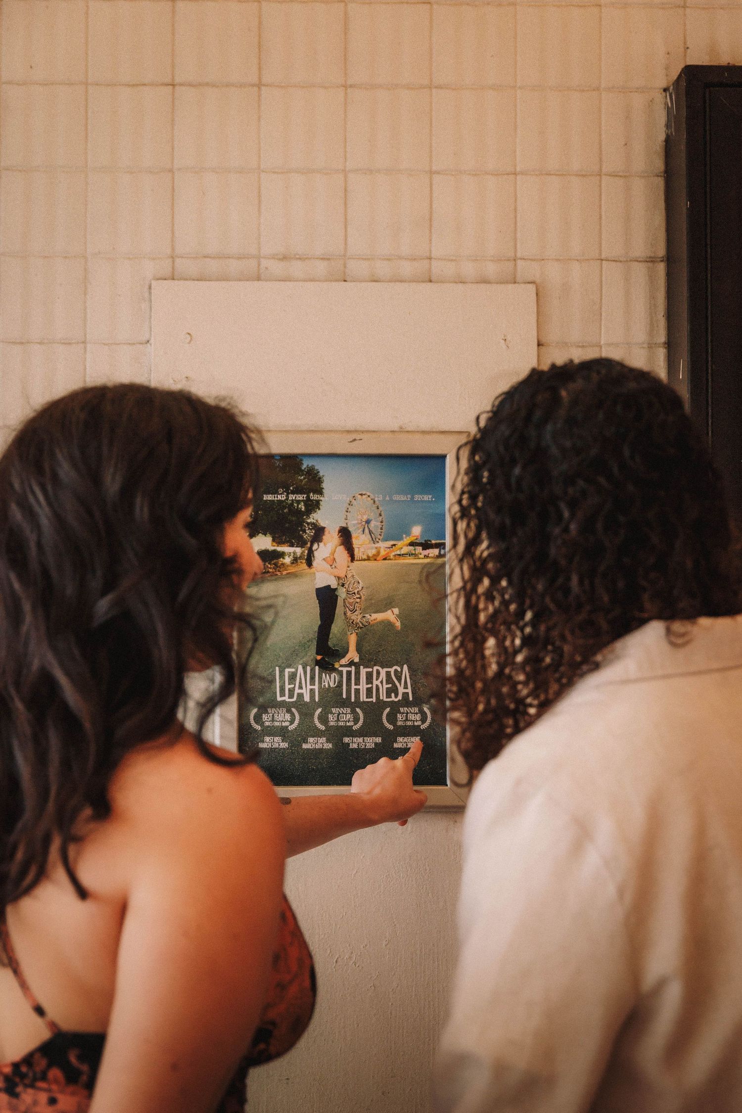 Newly engaged couple viewing a custom movie poster titled Leah and Theresa displayed on a theater wall.