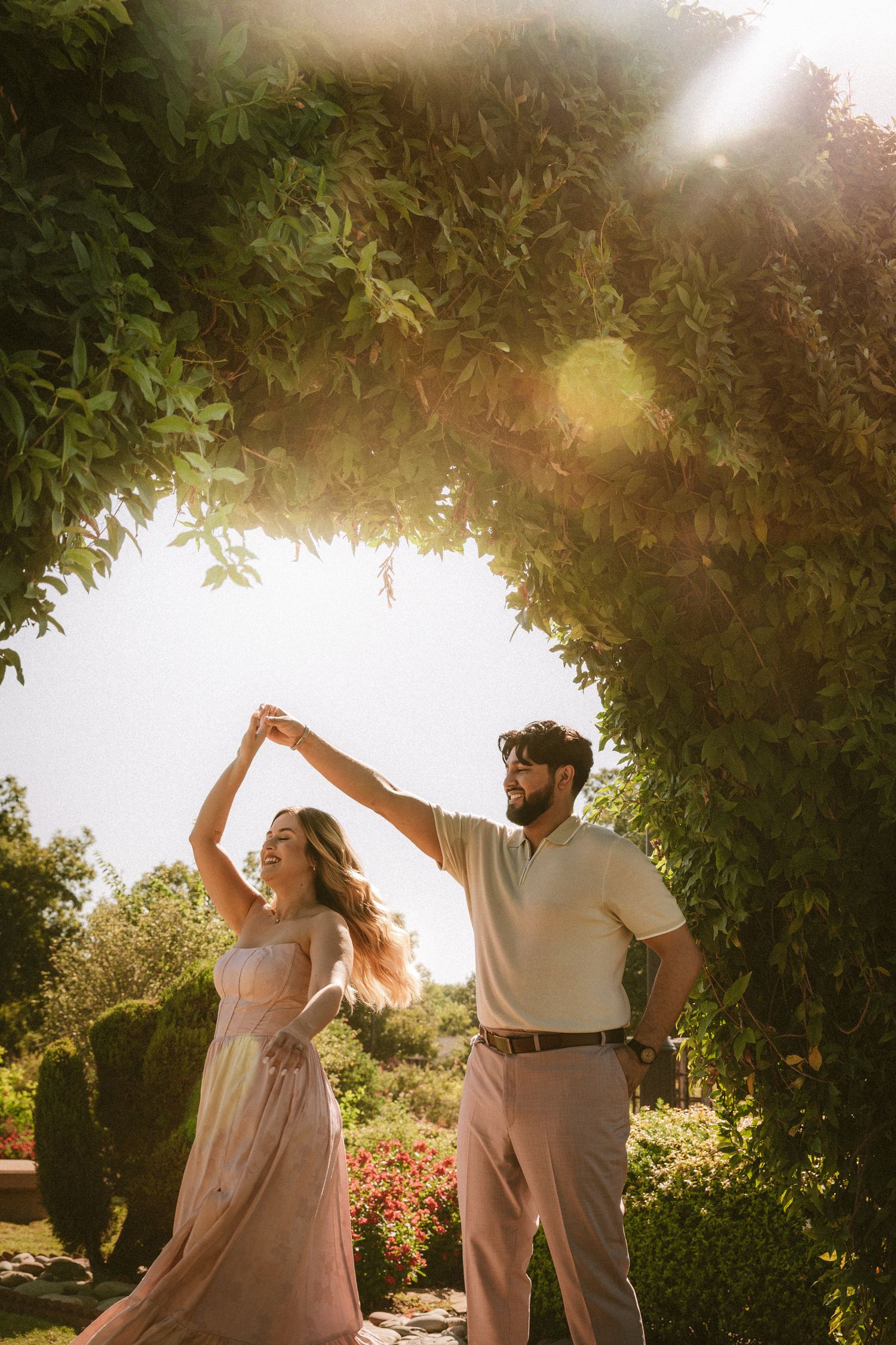 A couple dances together in a garden setting during golden hour, creating a romantic silhouette against the sunlight.