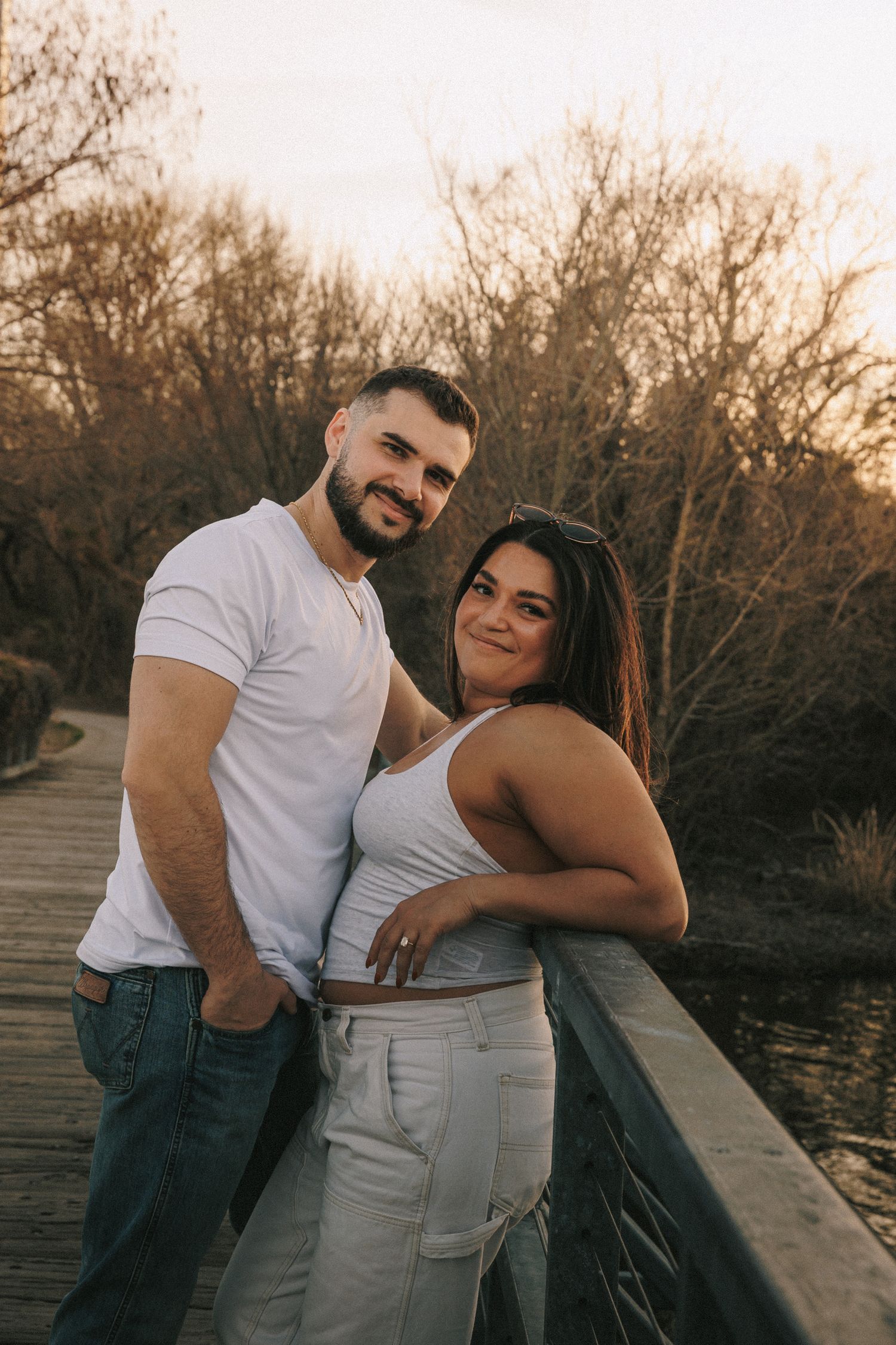 Romantic couple in white shirts embracing on a wooden dock during golden hour.