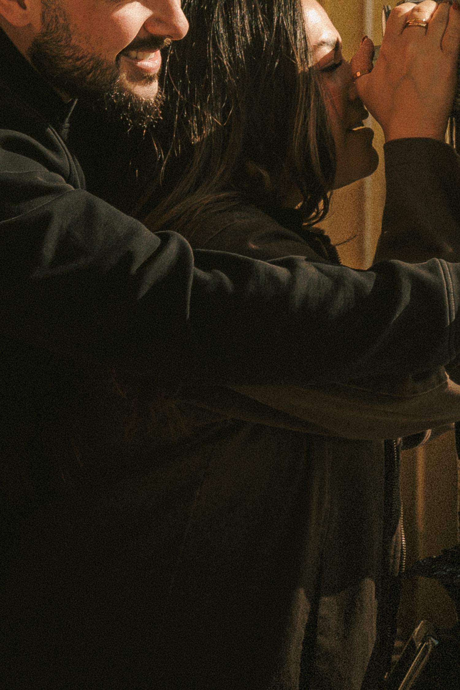 A close-up artistic shot showing an intimate moment between two people in dark clothing.