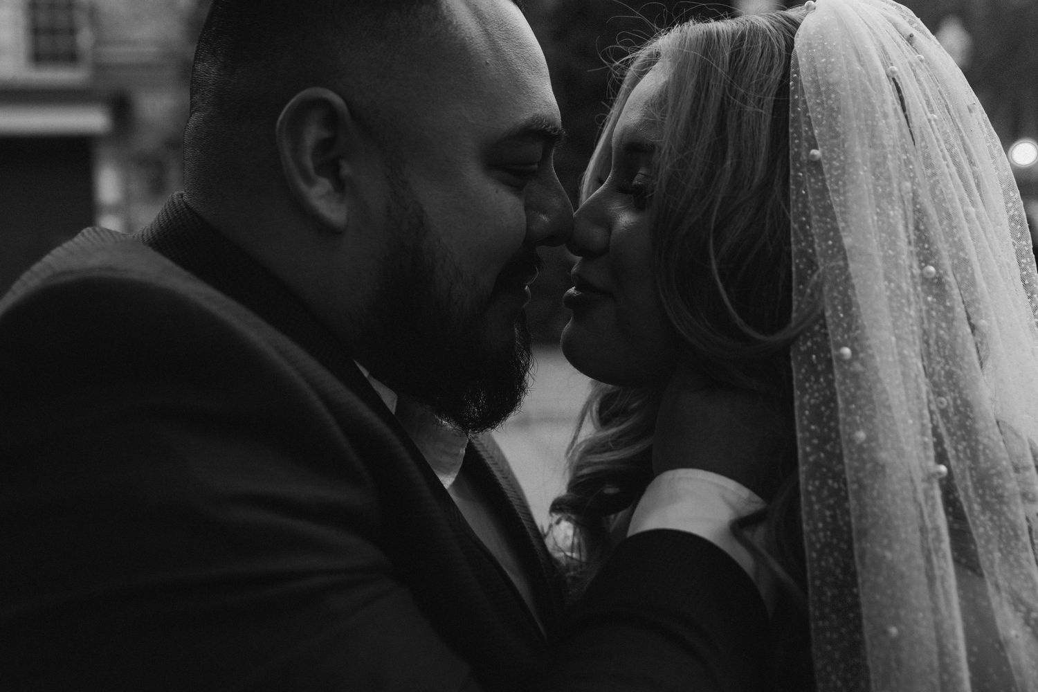 A couple in wedding attire share a tender moment together under a flowing white veil.