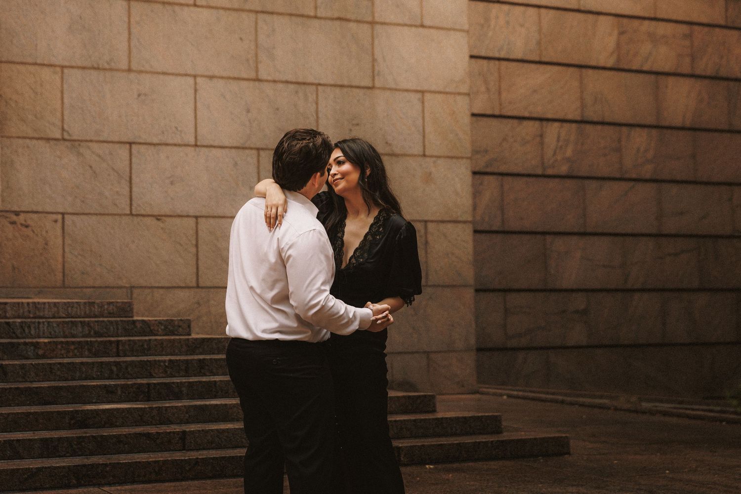 Couple embracing tenderly near stone steps and walls in an urban setting.