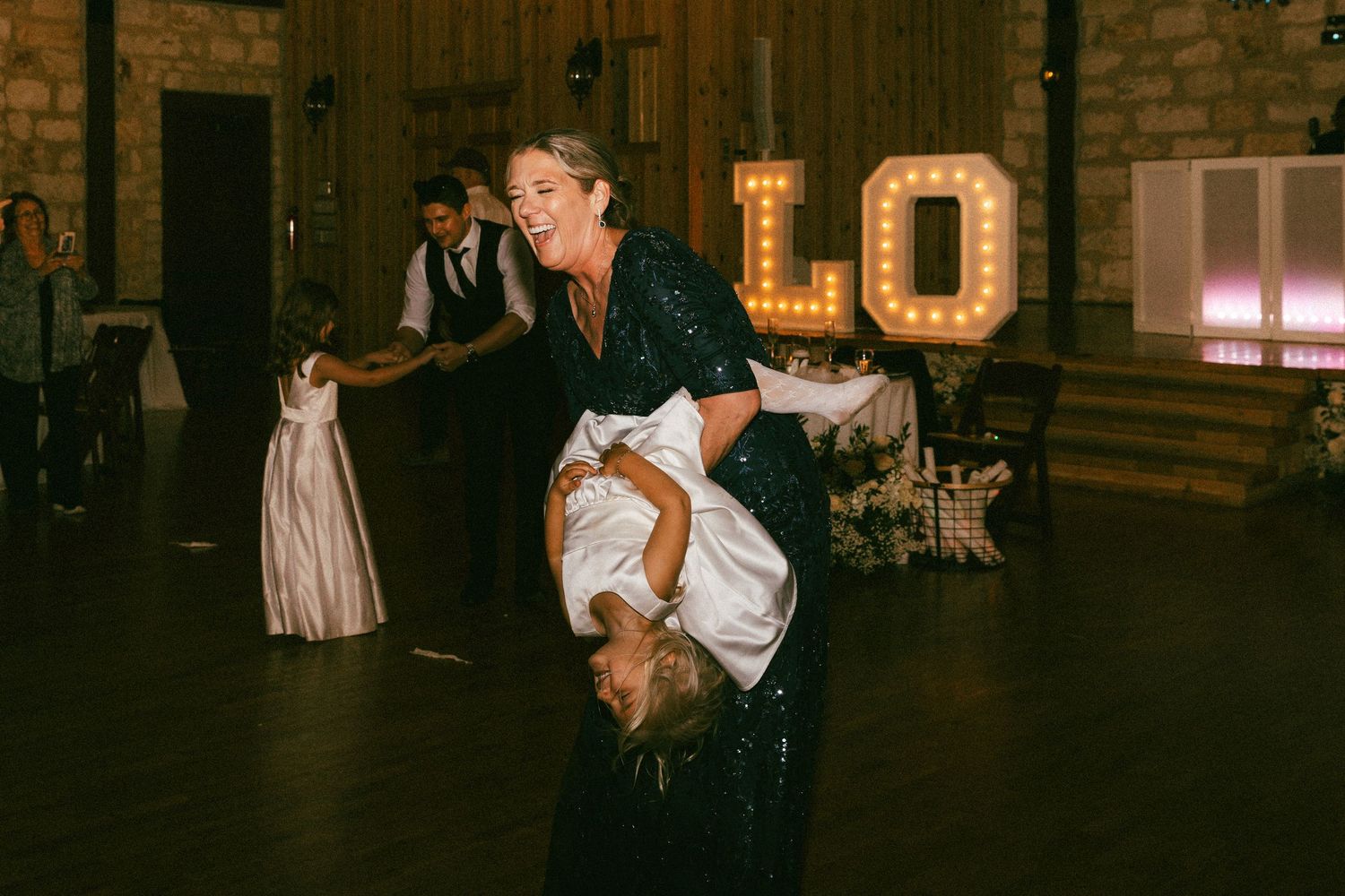 A woman in a sequin dress playfully dips the bride on a wedding reception dance floor.
