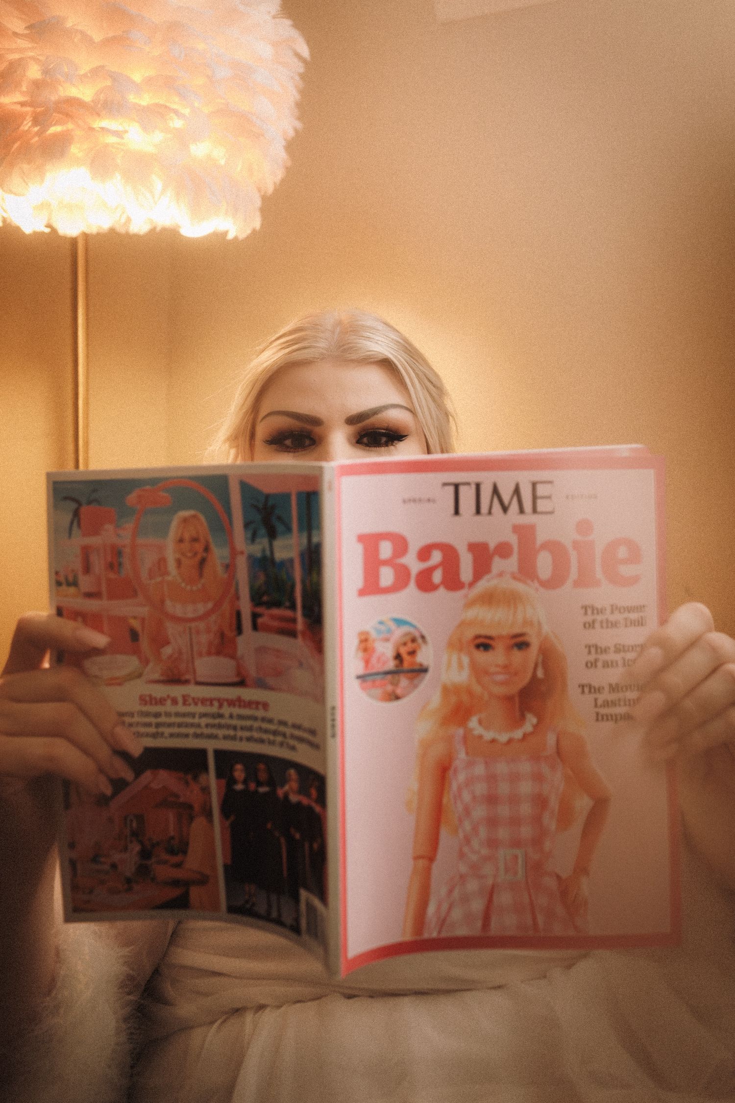 Blonde bride holding TIME Barbie magazine cover in front of her face in softly lit room.