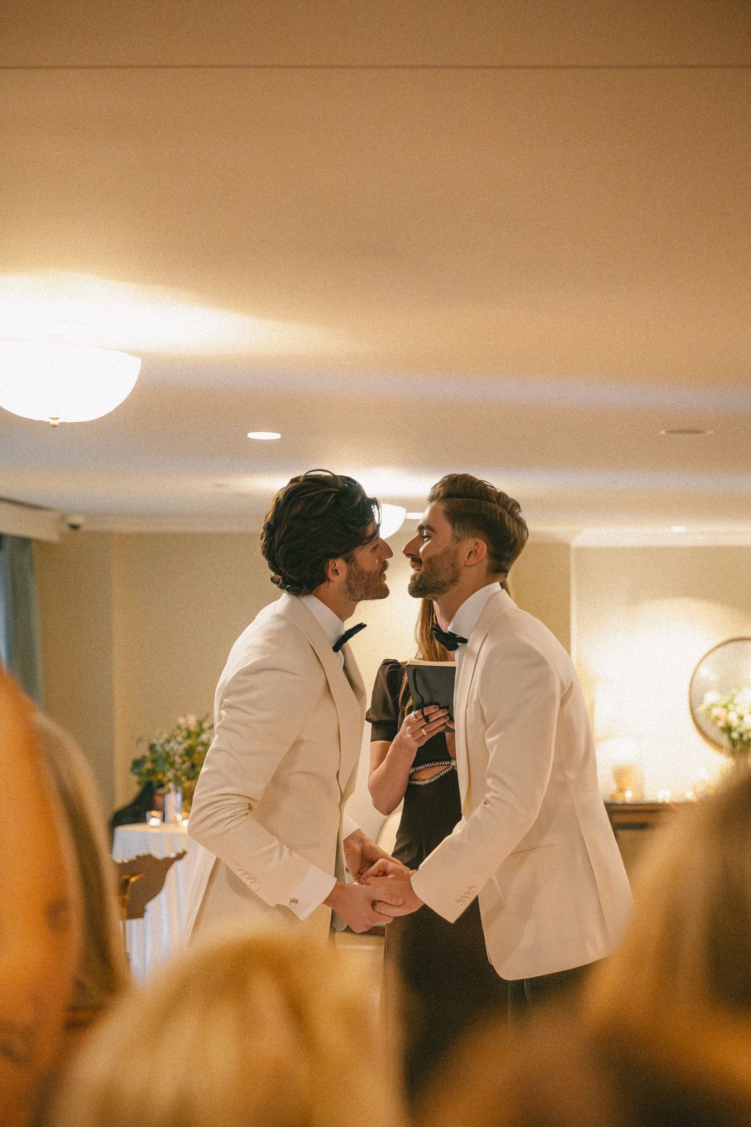 Two grooms in white tuxedos share a romantic moment together during their wedding ceremony.