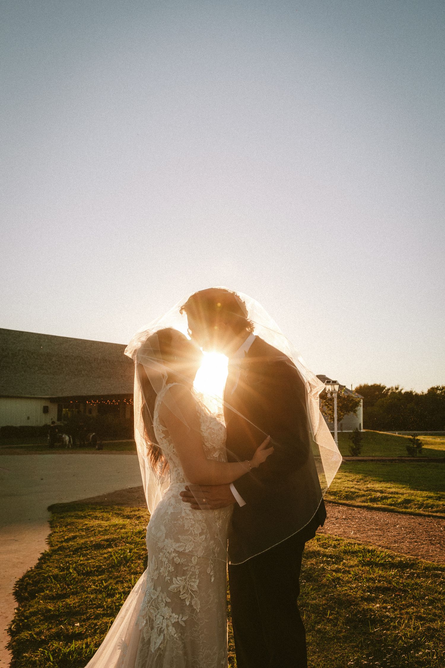 Bride and groom silhouetted kissing at golden sunset with wedding veil flowing in the breeze.
