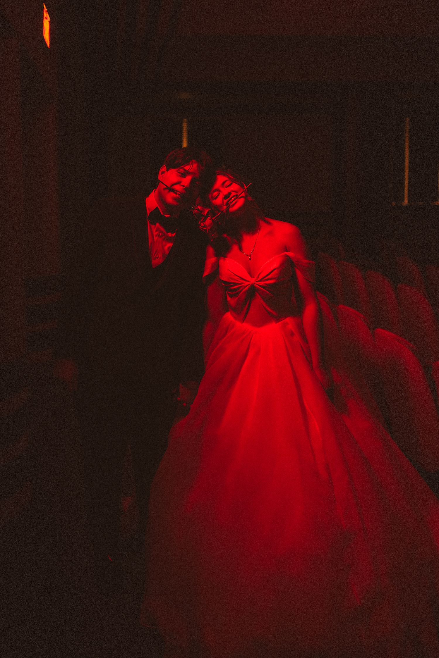 A woman in a dramatic red ball gown poses under intense red lighting in a dark theater.