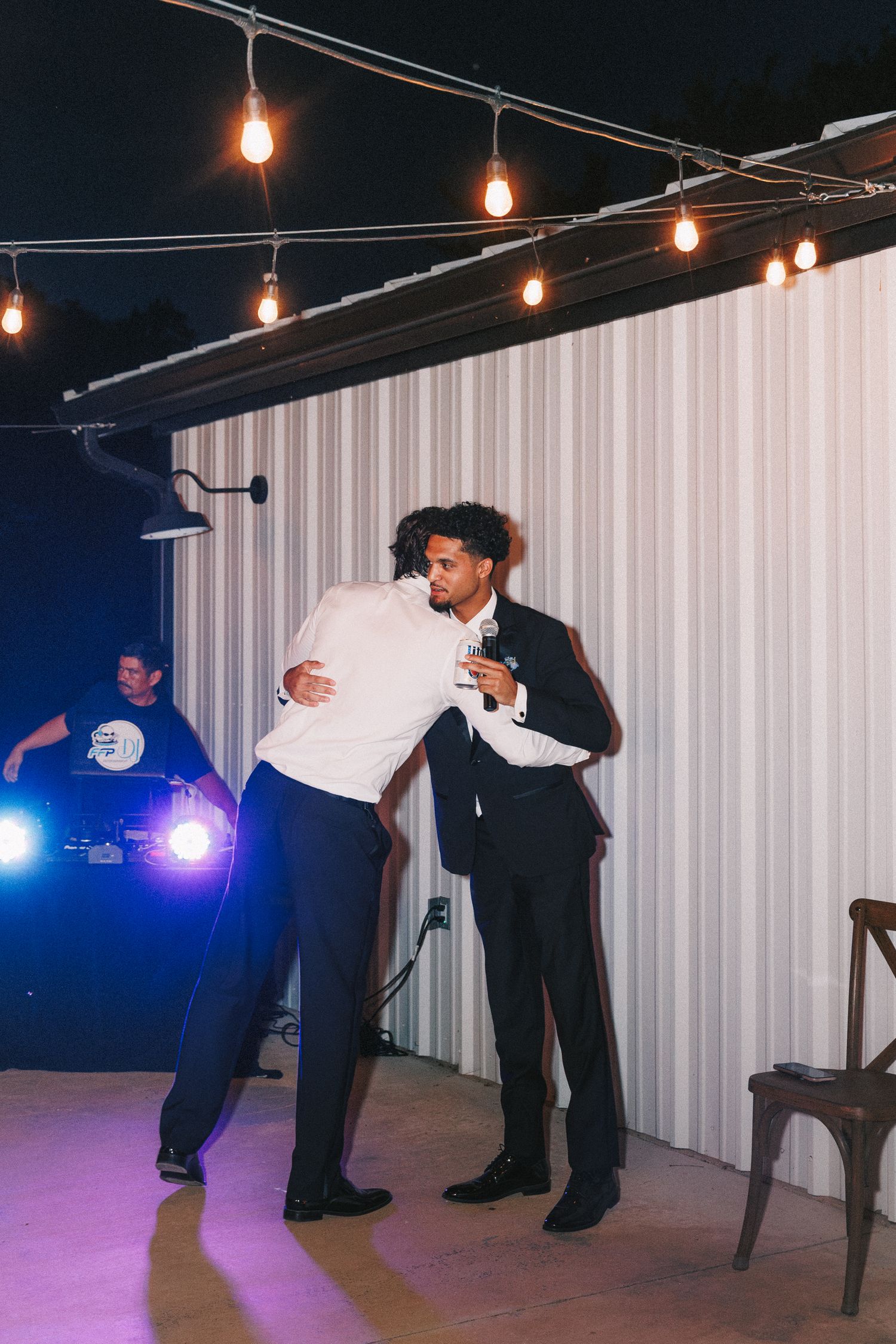 Two people embrace during a celebratory dance under warm string lights at an indoor venue.