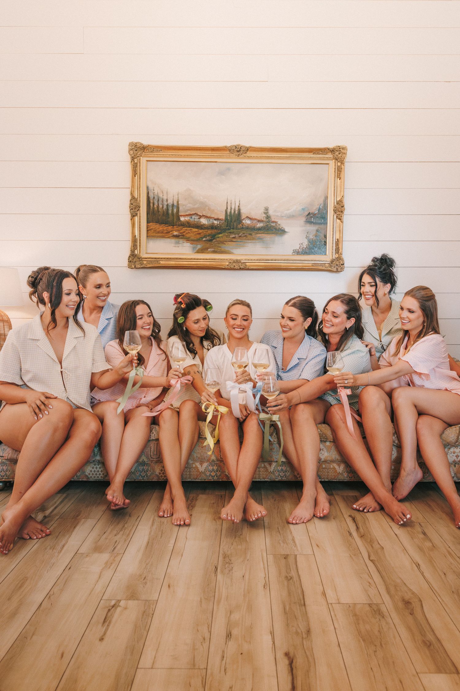 Group sitting together in matching robes on hardwood floor during wedding preparation.