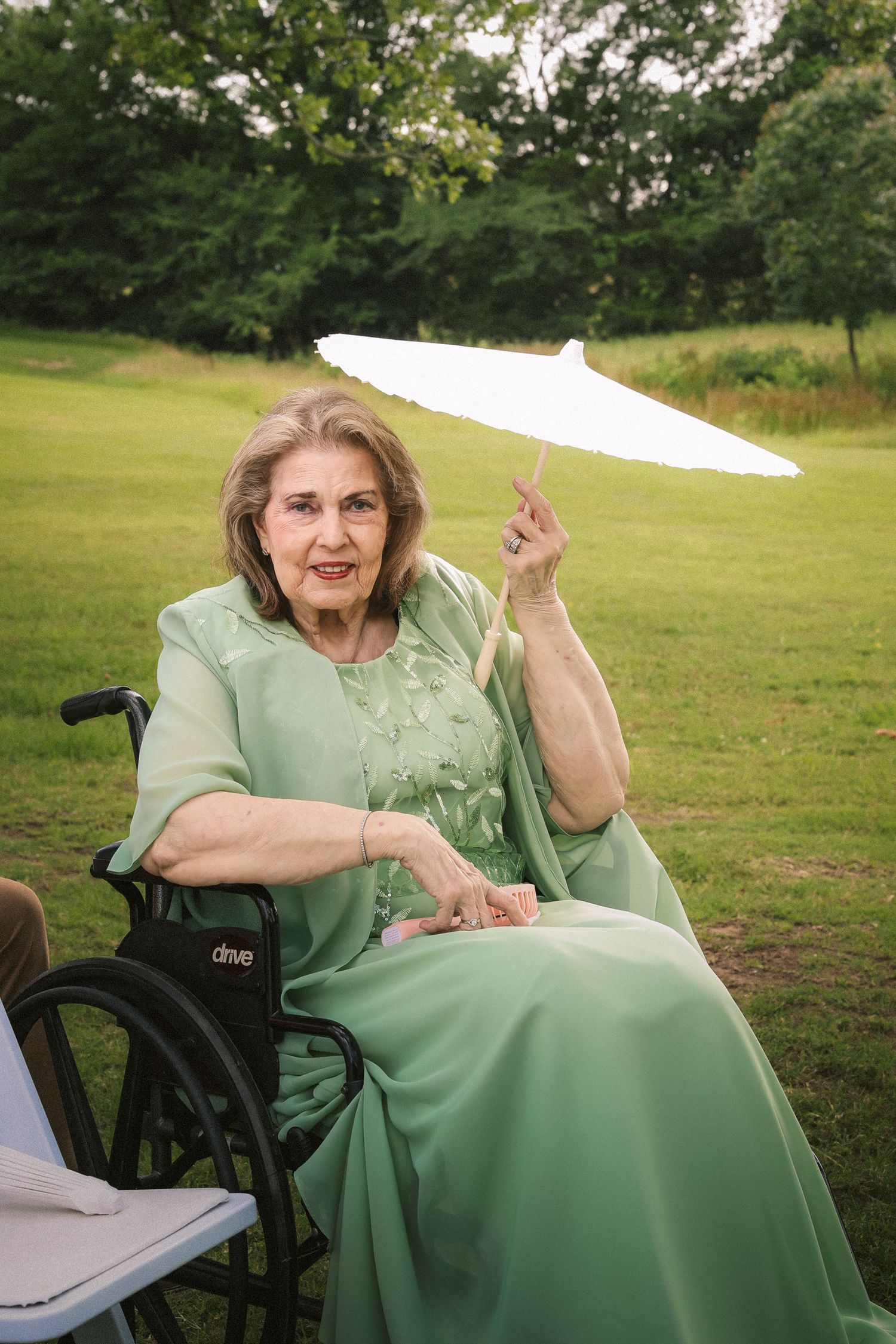 Person in mint green dress sitting with parasol in outdoor wedding setting.