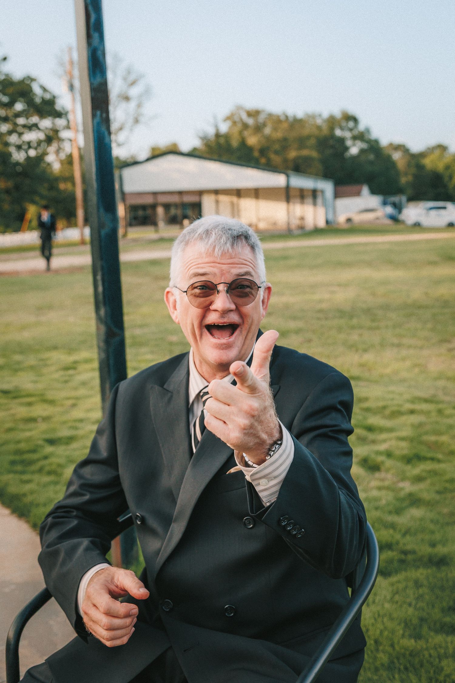 Senior gentleman in a dark suit laughing joyfully at an outdoor event.