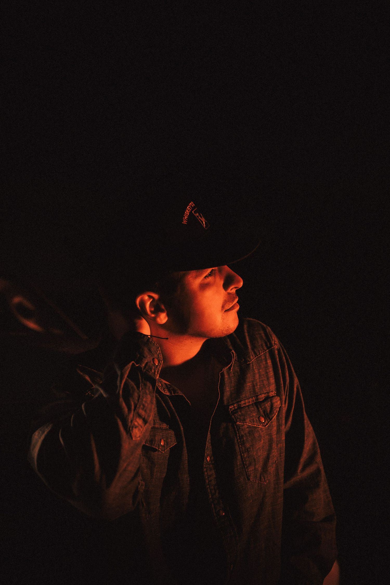 Silhouetted figures in dark clothing stand against a black background with dramatic orange lighting.