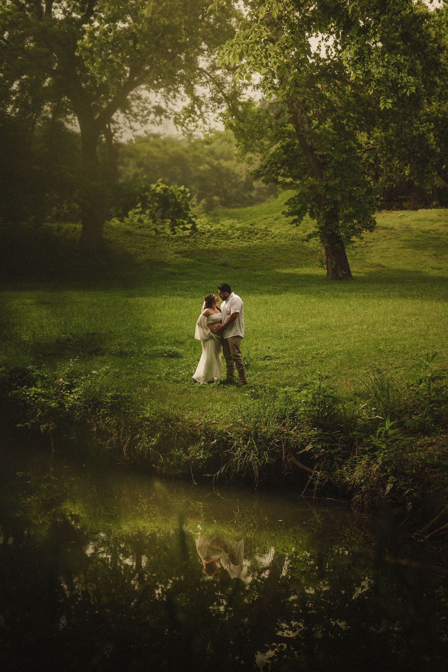 Beautiful romantic scene by a tranquil pond with green meadow and trees reflecting in still water at sunset.