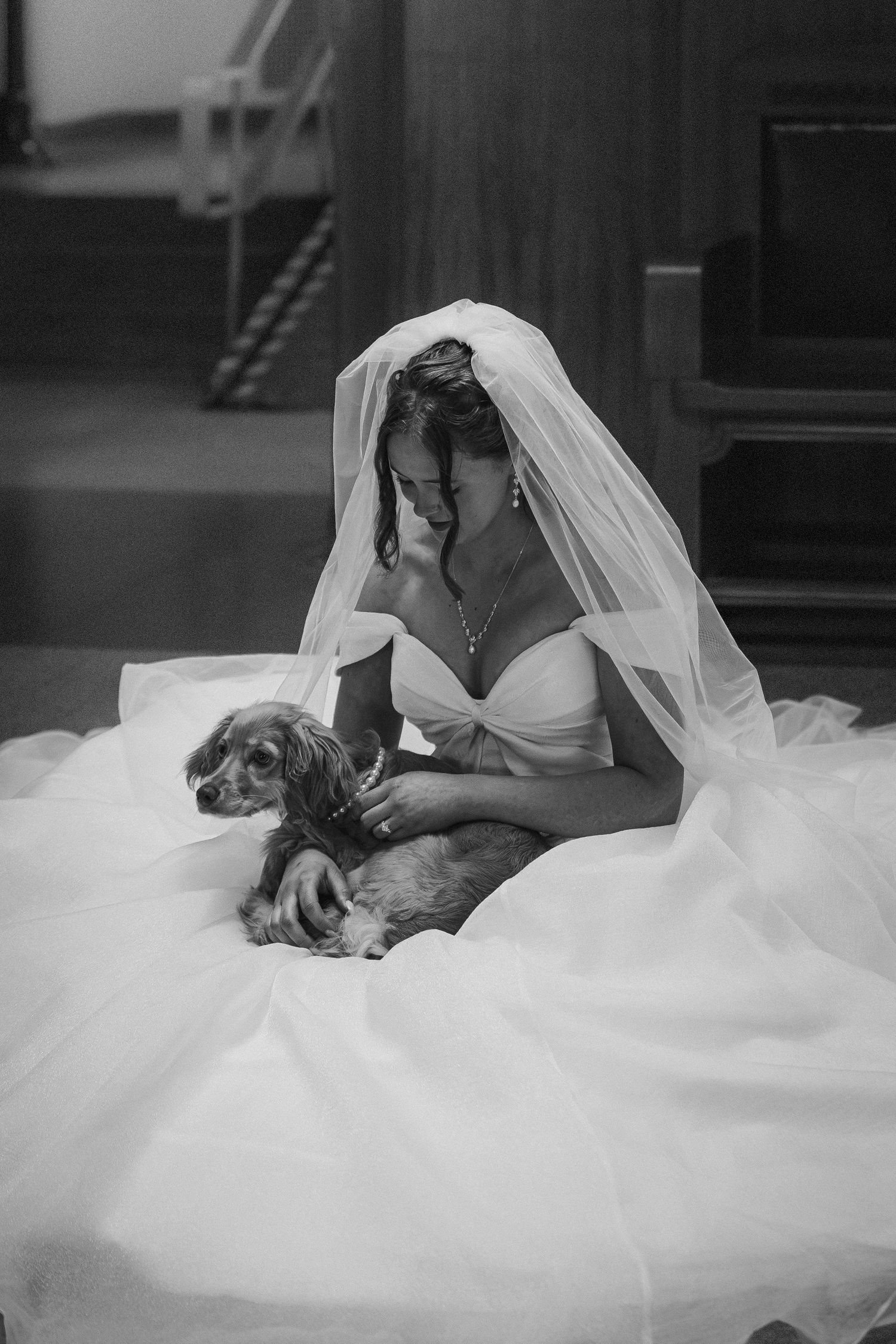 Black and white photo of smiling bride in white gown and veil cuddling small dog.
