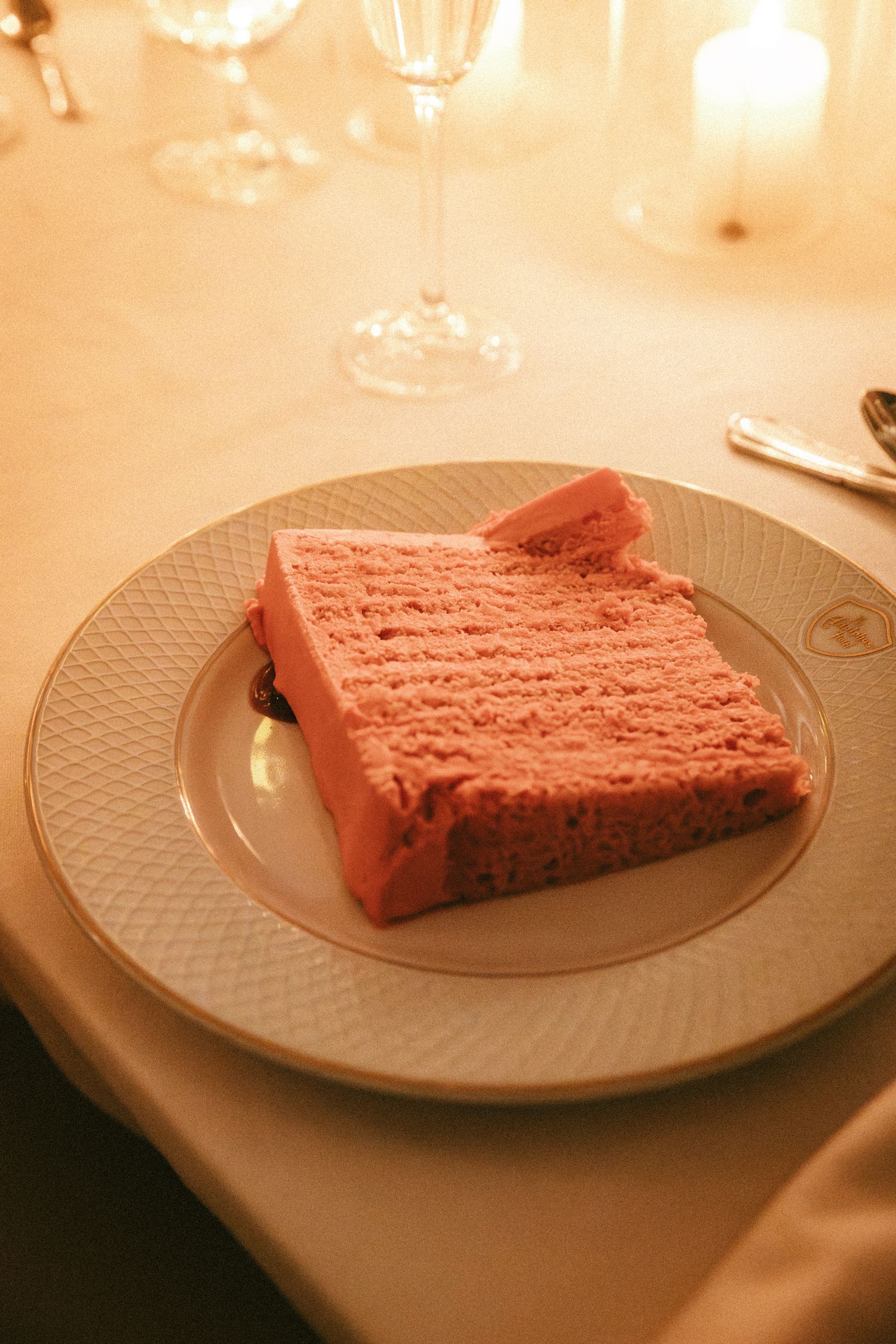 Slice of pink wedding cake with textured frosting served on elegant white plate.