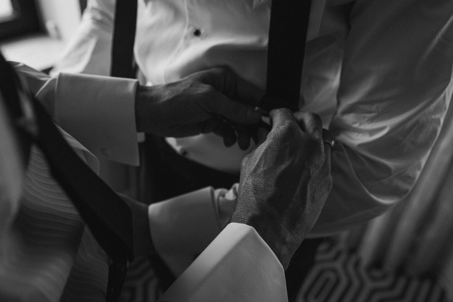 Black and white close-up of two grooms helping each other with bow ties on wedding day.