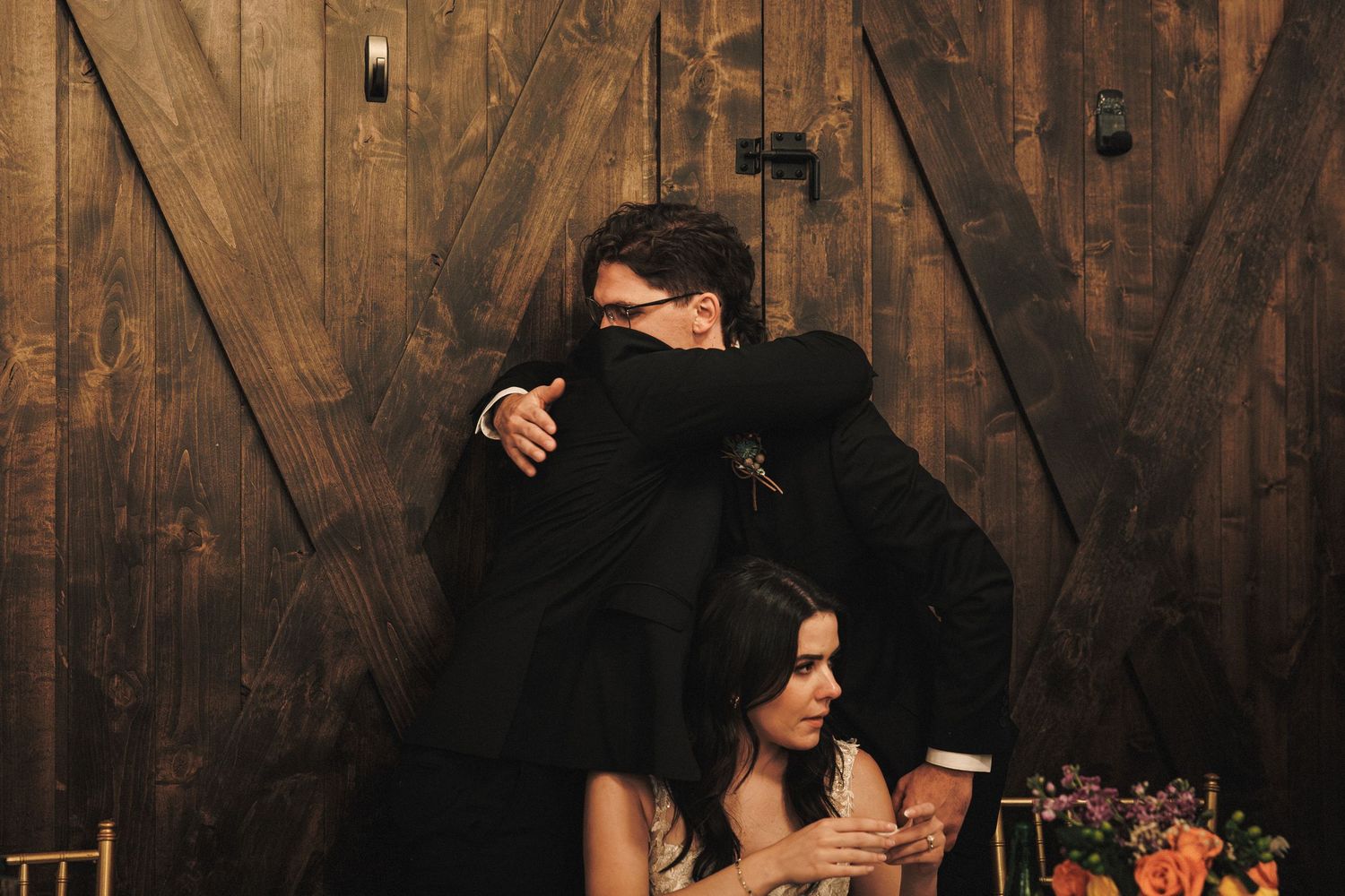 Emotional groom receives a heartfelt hug from a guest at rustic barn wedding reception.