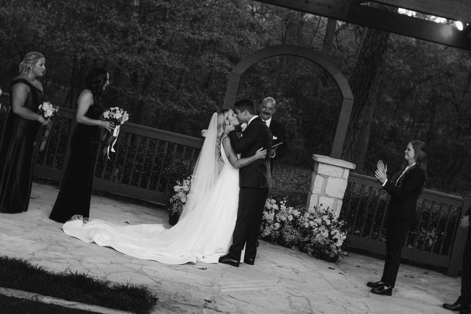 Black and white photo of a bride and groom sharing their first kiss at the altar.