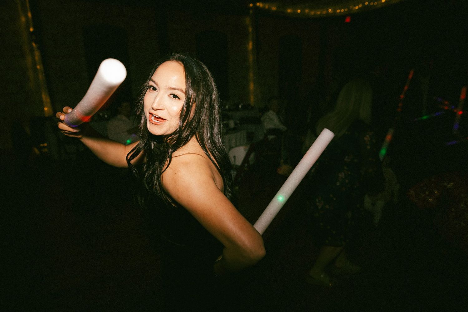 Smiling wedding guest dancing with glow sticks at lively evening wedding reception celebration.