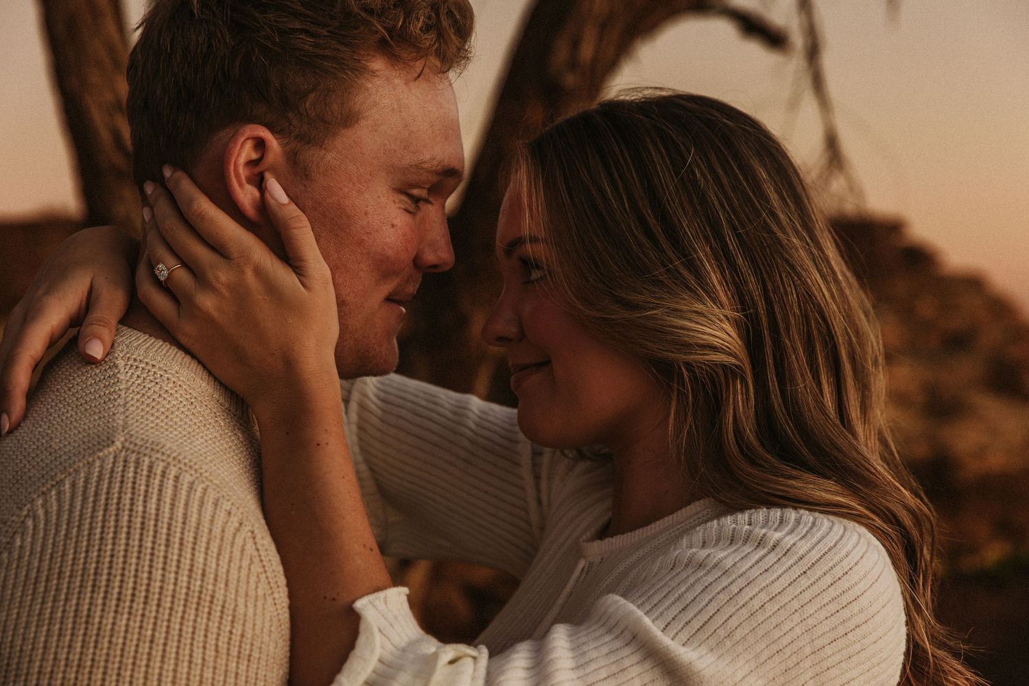 A tender close-up of a couple in cream sweaters sharing an intimate moment at dusk.