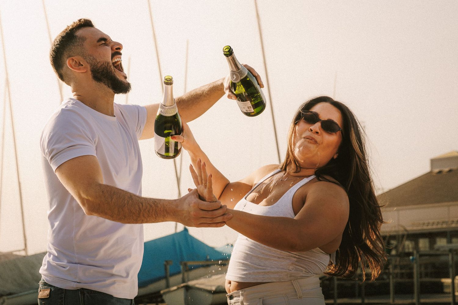 A couple shares champagne and laughter on a dock during golden hour.