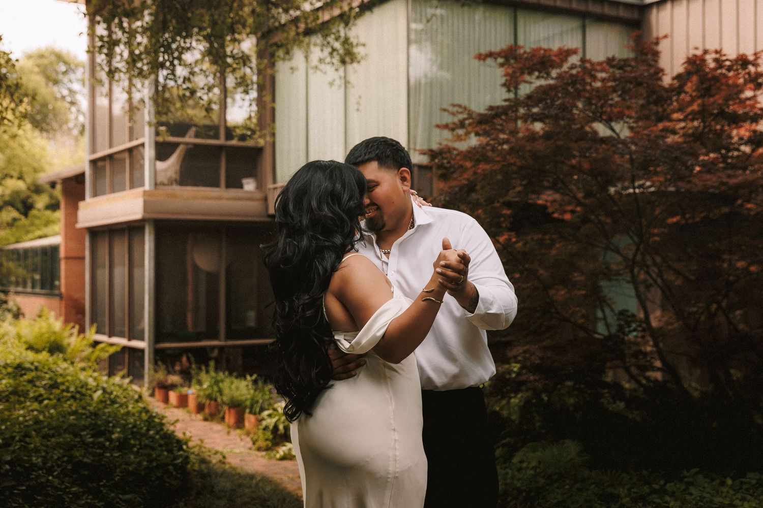 Newlyweds share an intimate dance together in a beautiful garden setting surrounded by fall foliage.