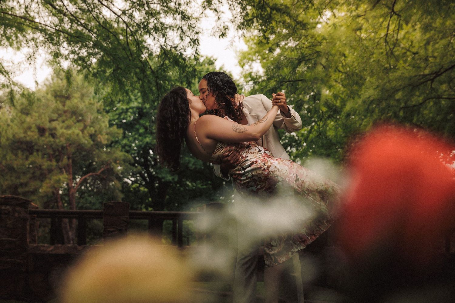 Golden hour sunlight filters through trees at an outdoor wedding ceremony with guests gathered on wooden benches.
