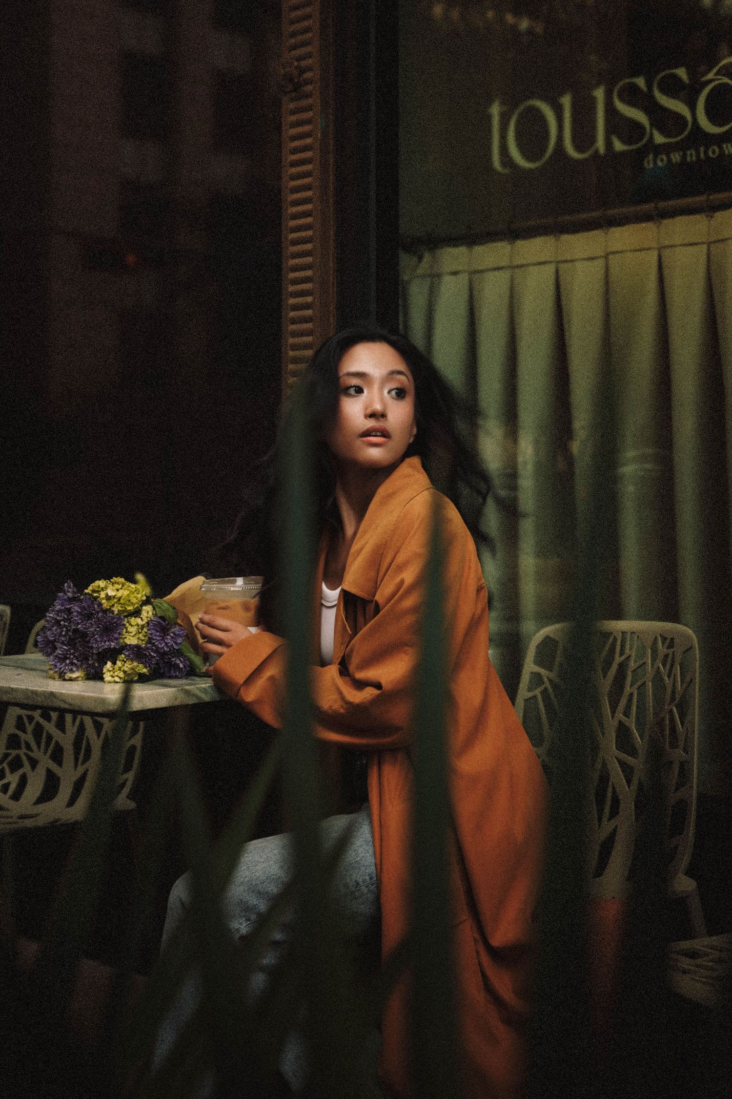A figure in an orange kimono sits contemplatively in a dark atmospheric setting near illuminated signage.
