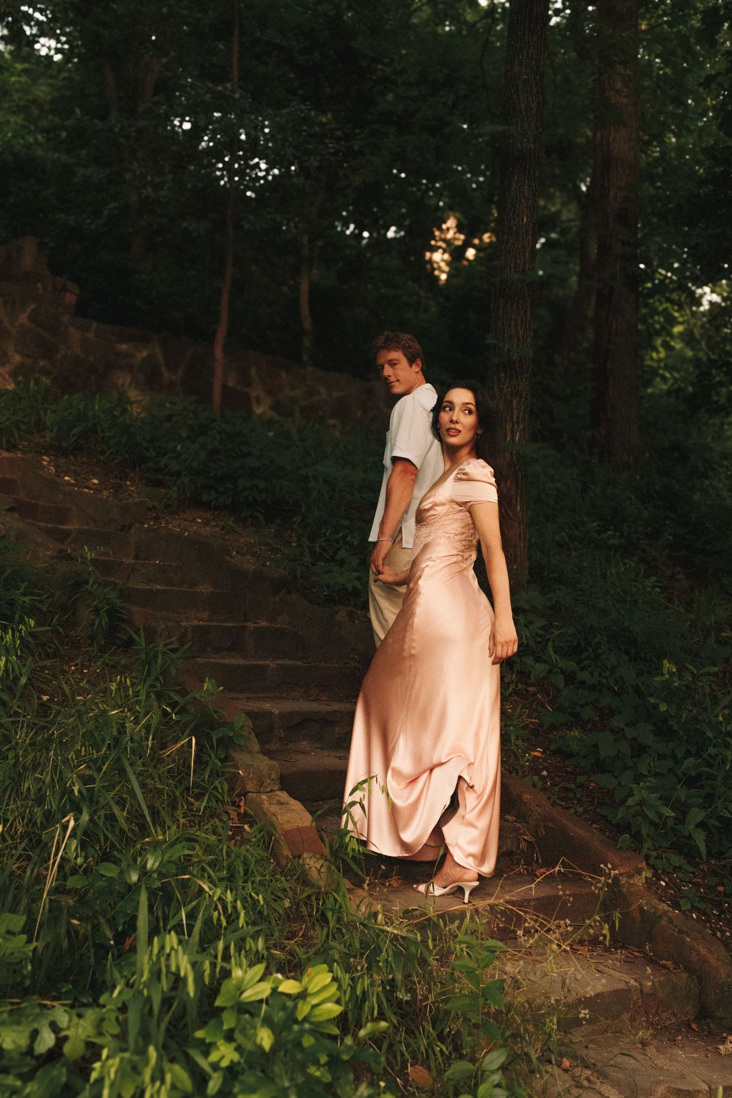 A sequence of photos showing someone in a light pink dress walking down stone steps in a wooded garden setting at dusk.