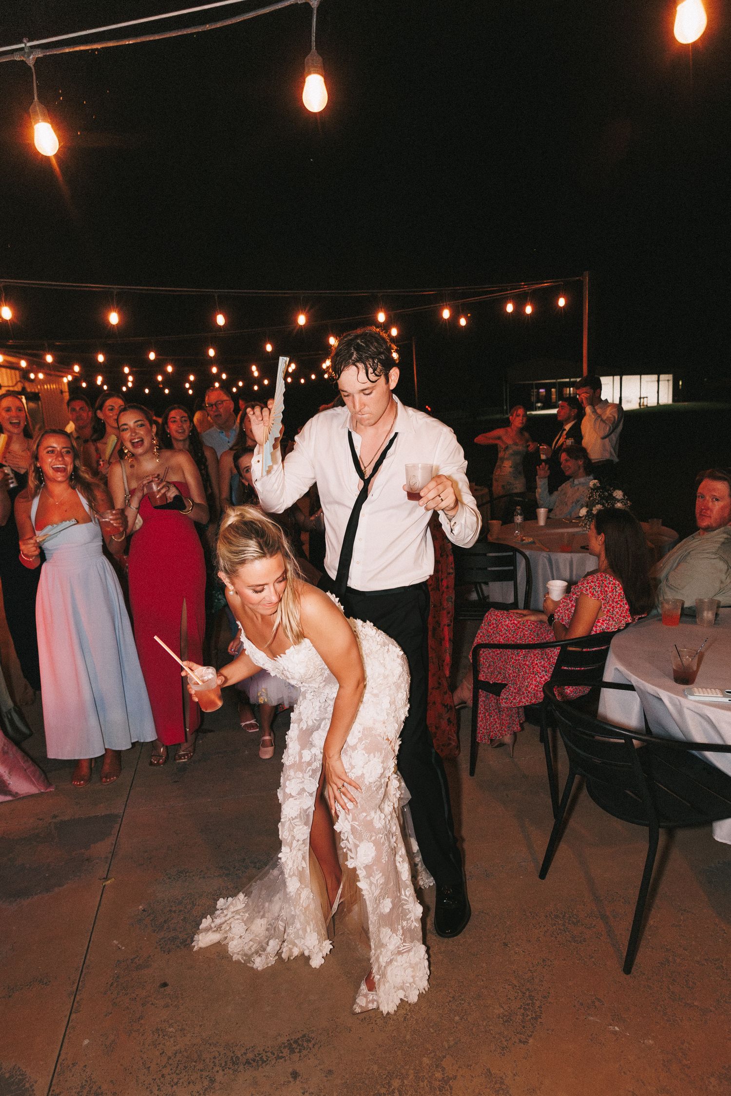 Lively wedding reception scene with dancing under string lights on outdoor patio.