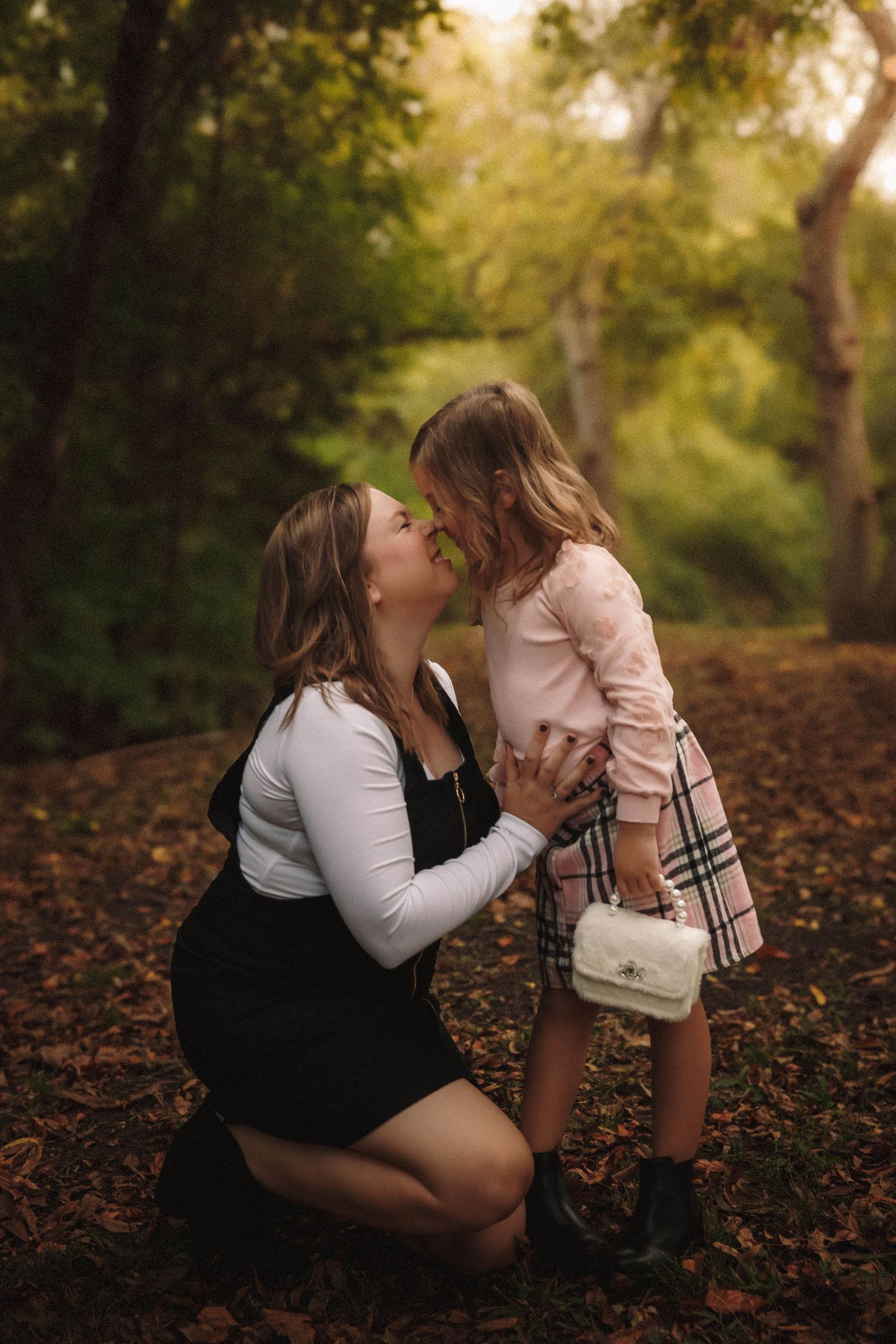 Tender autumn moment captured between parent and child among fallen leaves in a sunlit forest setting.