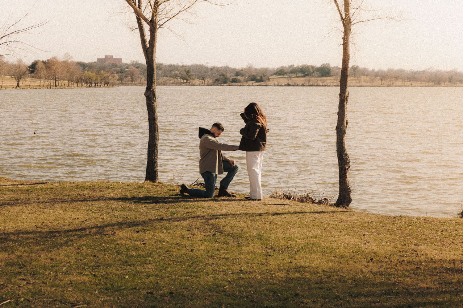 A couple sits on a bench by a serene lake during sunset, creating a peaceful autumn scene.