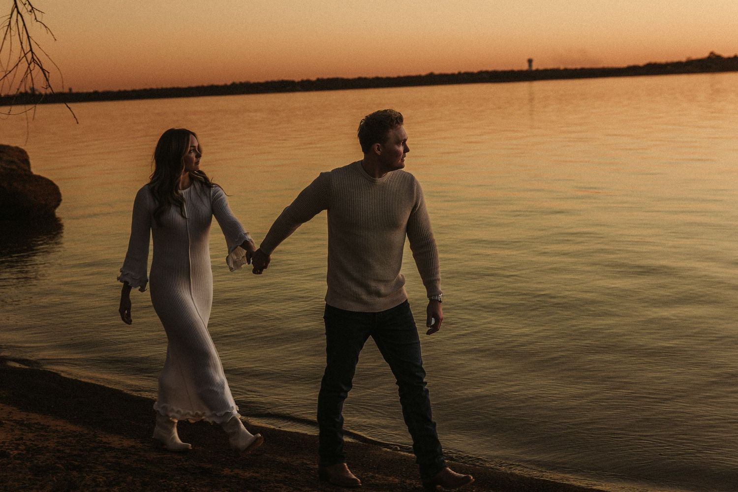 Silhouettes of couple walking along waterfront during golden hour.
