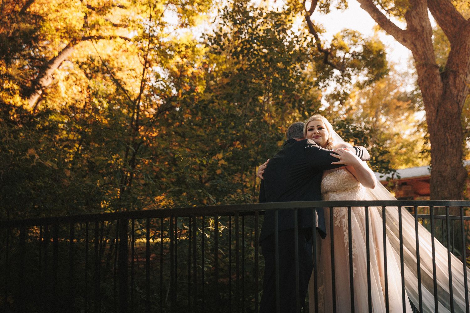 Bride and groom embracing on a bridge surrounded by golden autumn trees at an outdoor wedding.