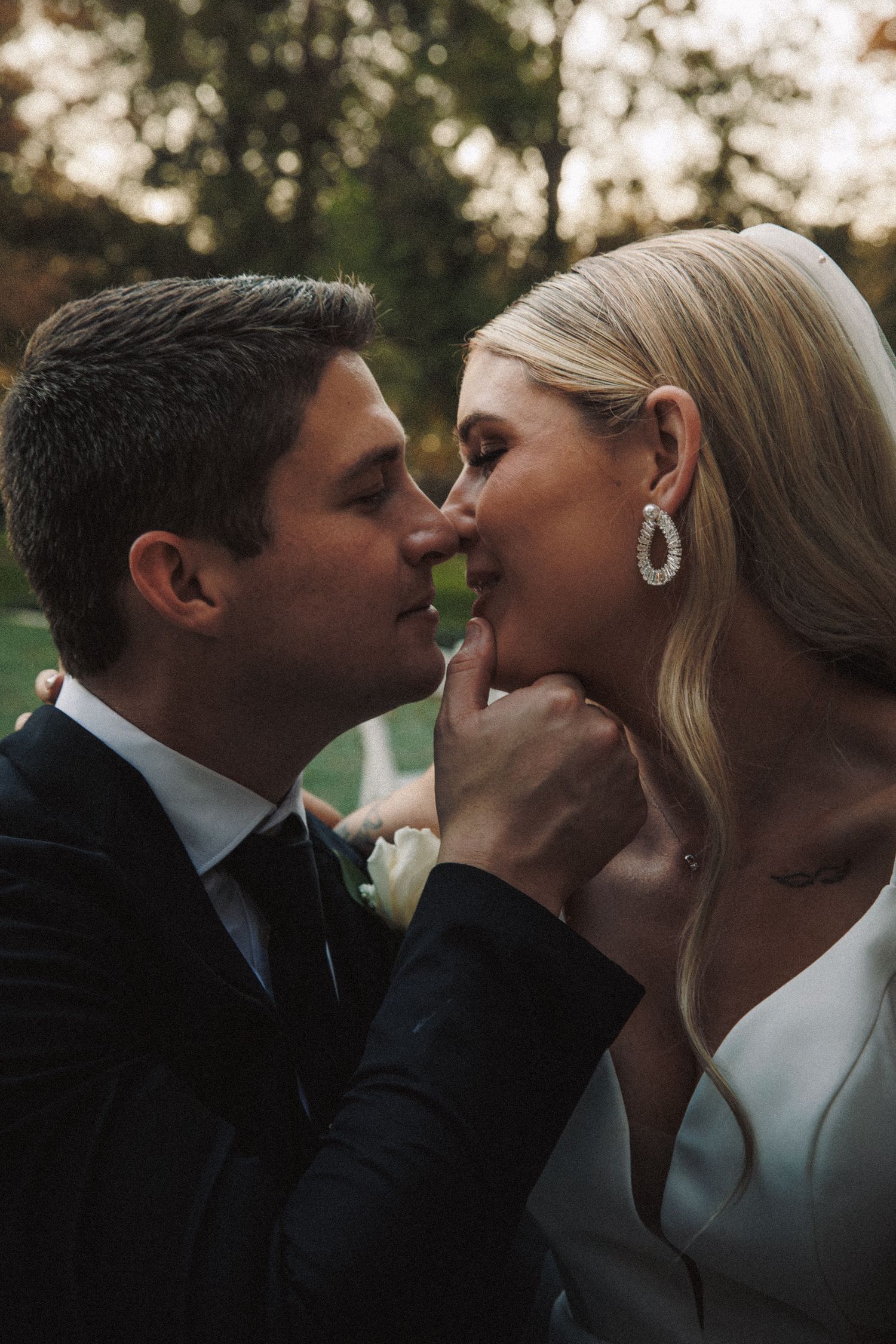 A groom tenderly holds his brides chin as they share an intimate moment at their fall outdoor wedding.