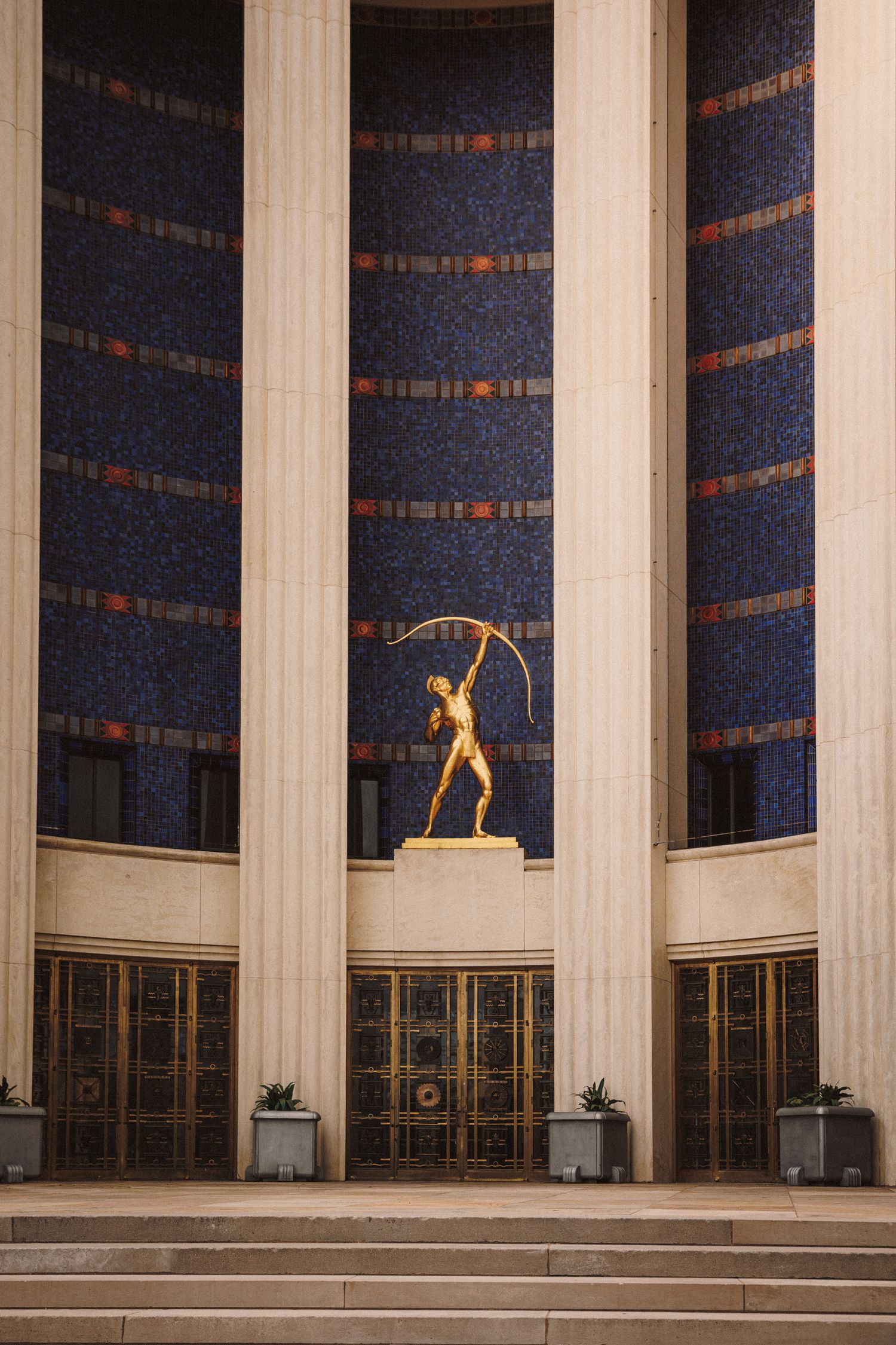 Art Deco building facade with golden archer statue between ornate mosaic columns.