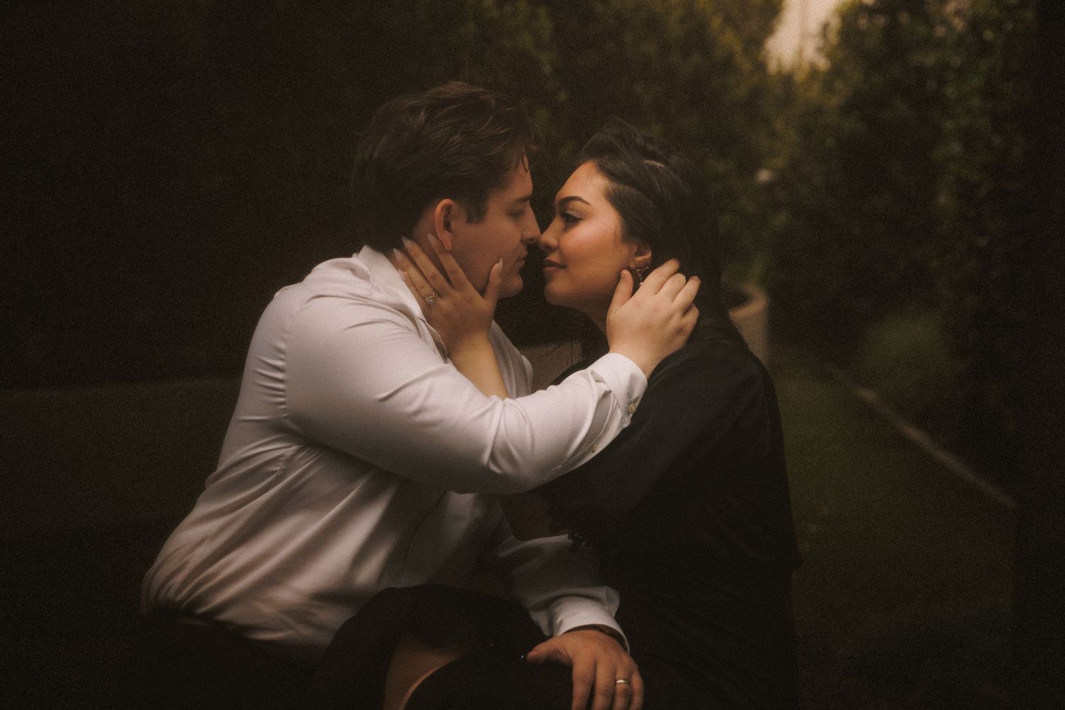 A couple shares a passionate kiss outdoors in a warmly lit romantic setting at dusk.