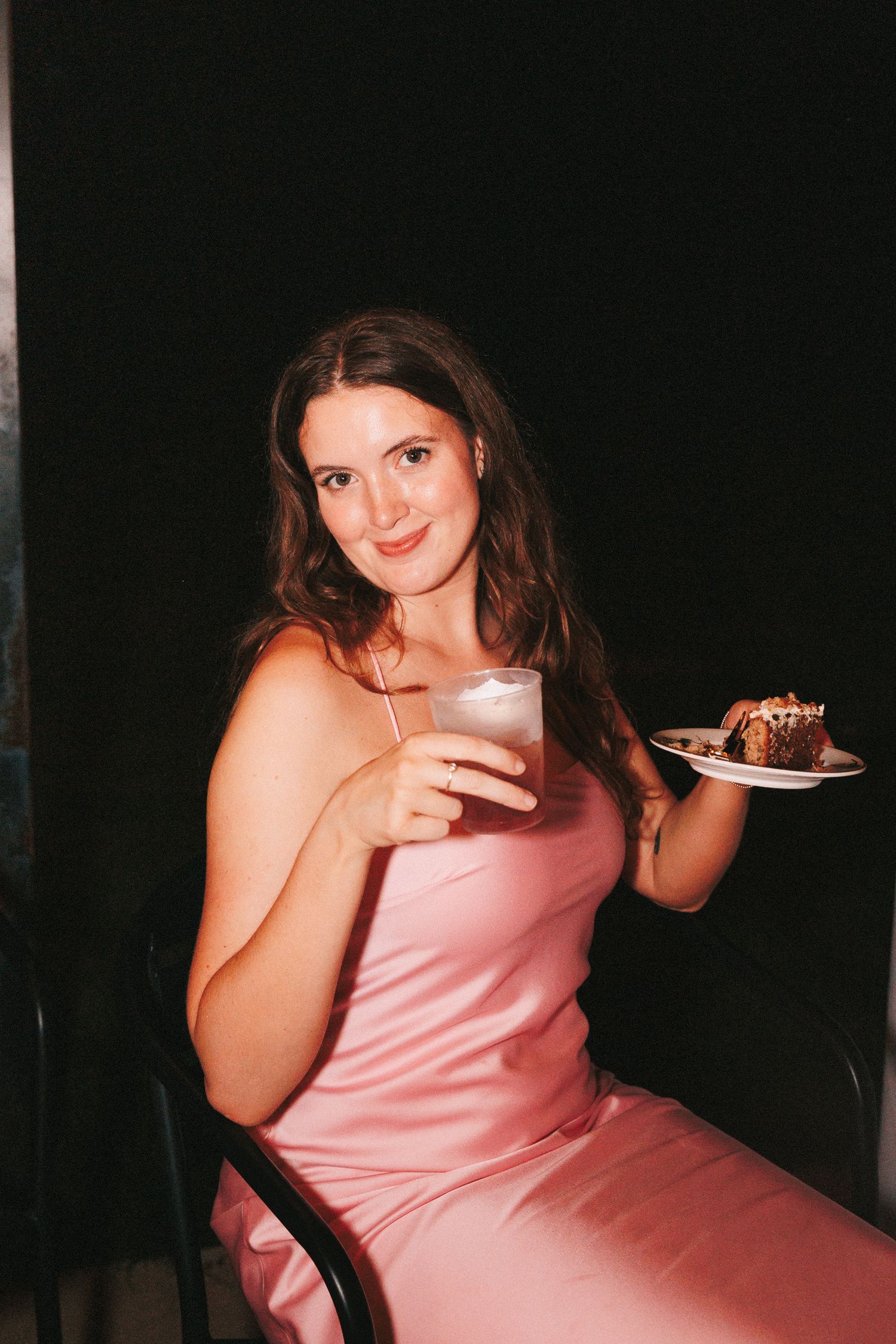 Person in pink dress sitting casually while enjoying dessert.