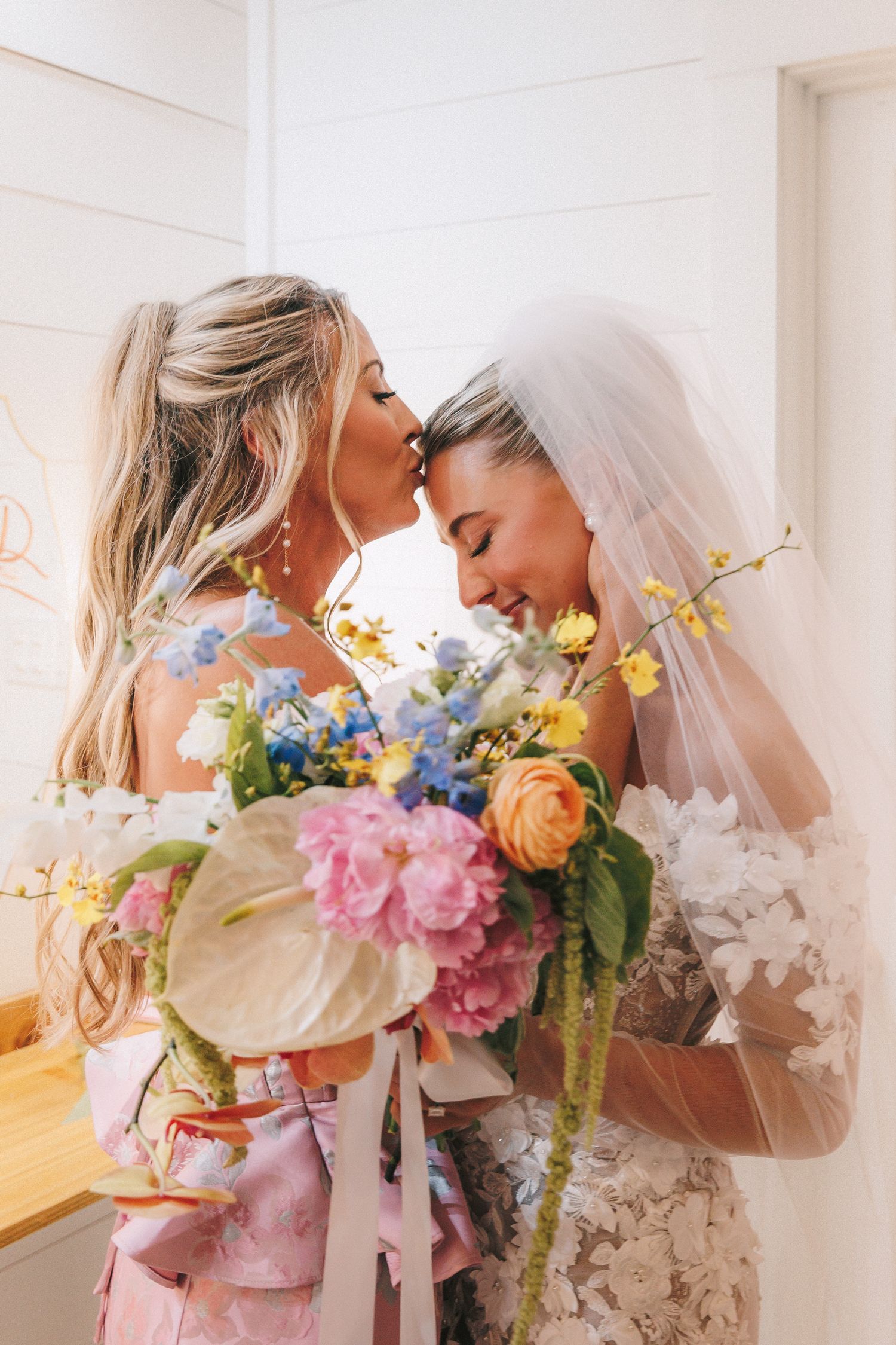 Two figures embrace while holding a vibrant bouquet of pink, orange and blue flowers.