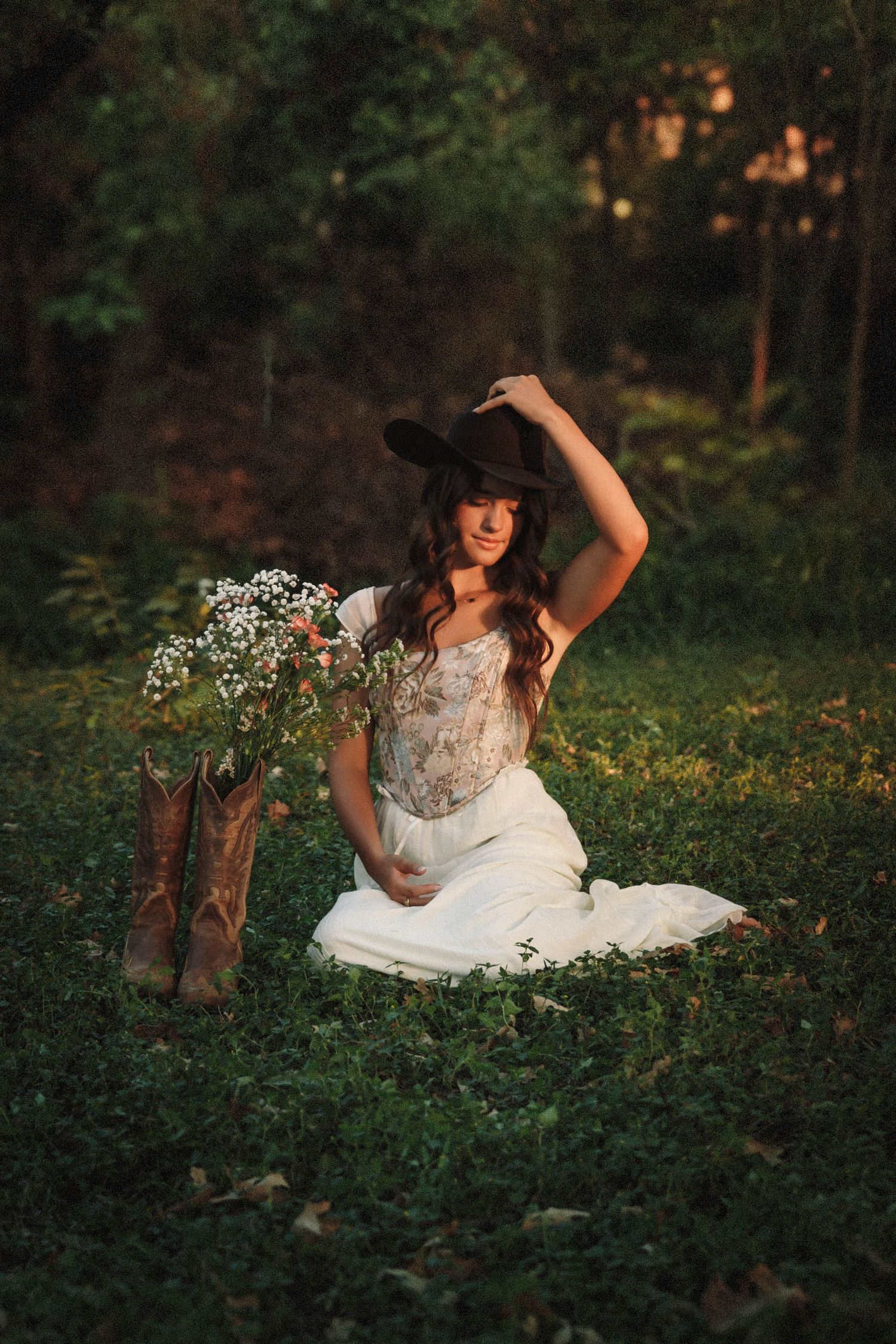 A bride in a white lace dress poses gracefully in a lush garden setting during golden hour.